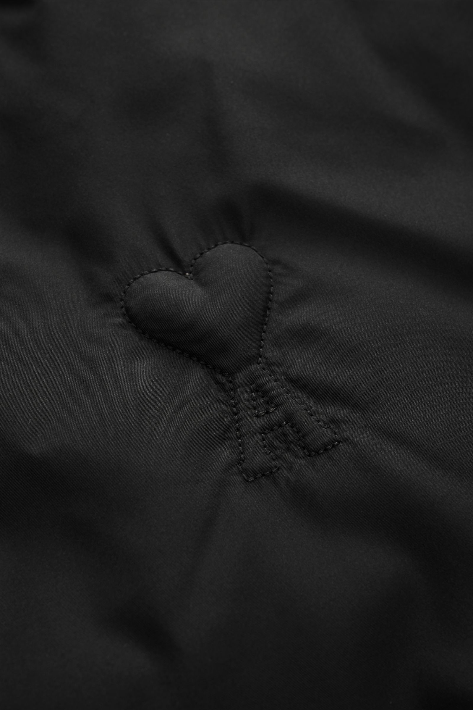 Nahaufnahme der gesteppten Logo-Prägung auf der Brust der Ami Paris Daunenjacke schwarz aus hochwertiger Microfaser.