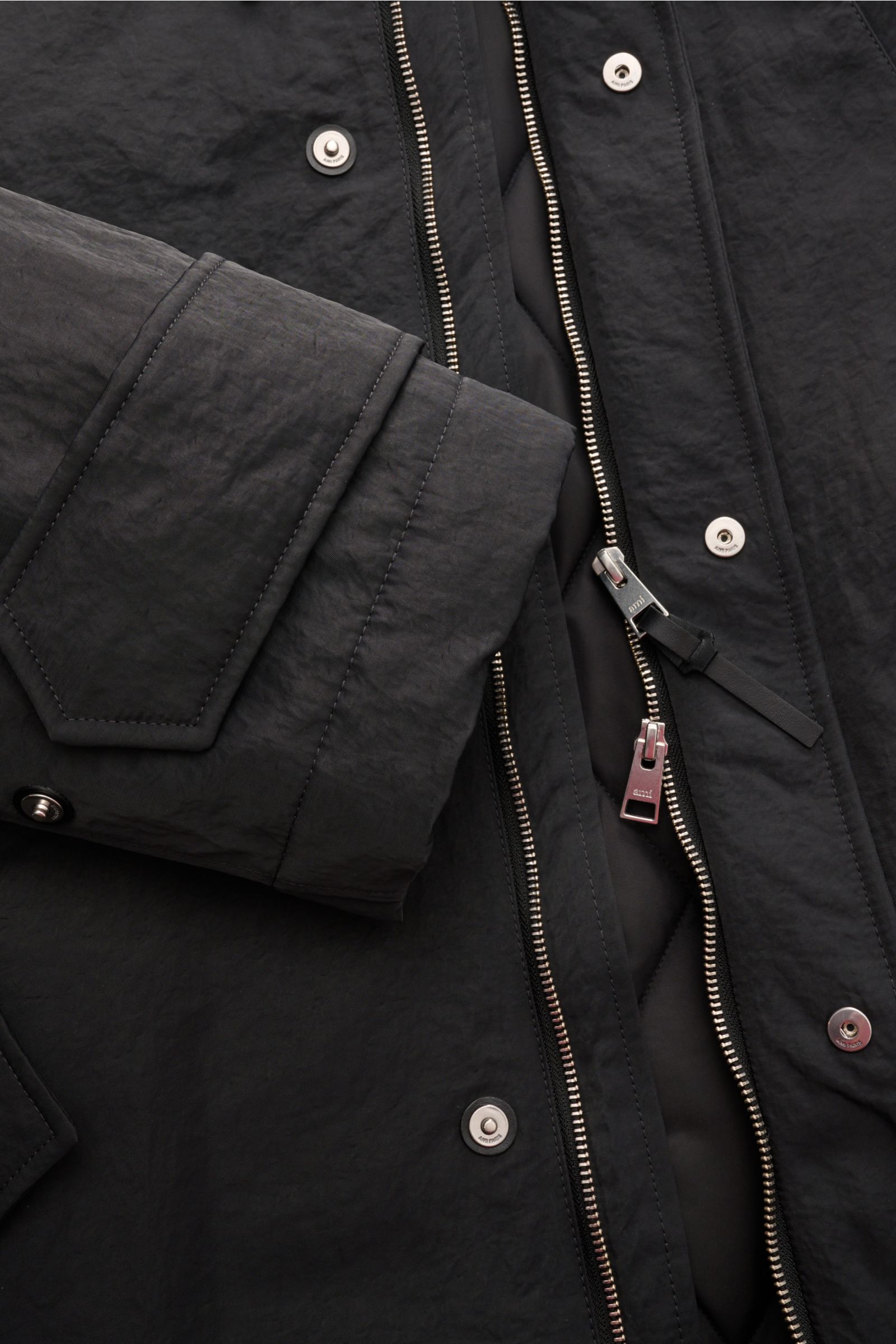 Nahaufnahme des Ami Paris Parka anthrazit aus wasserabweisendem Crinkle-Serge, mit Zwei-Wege-Reißverschluss, Knöpfen und gesteppter Innenansicht.