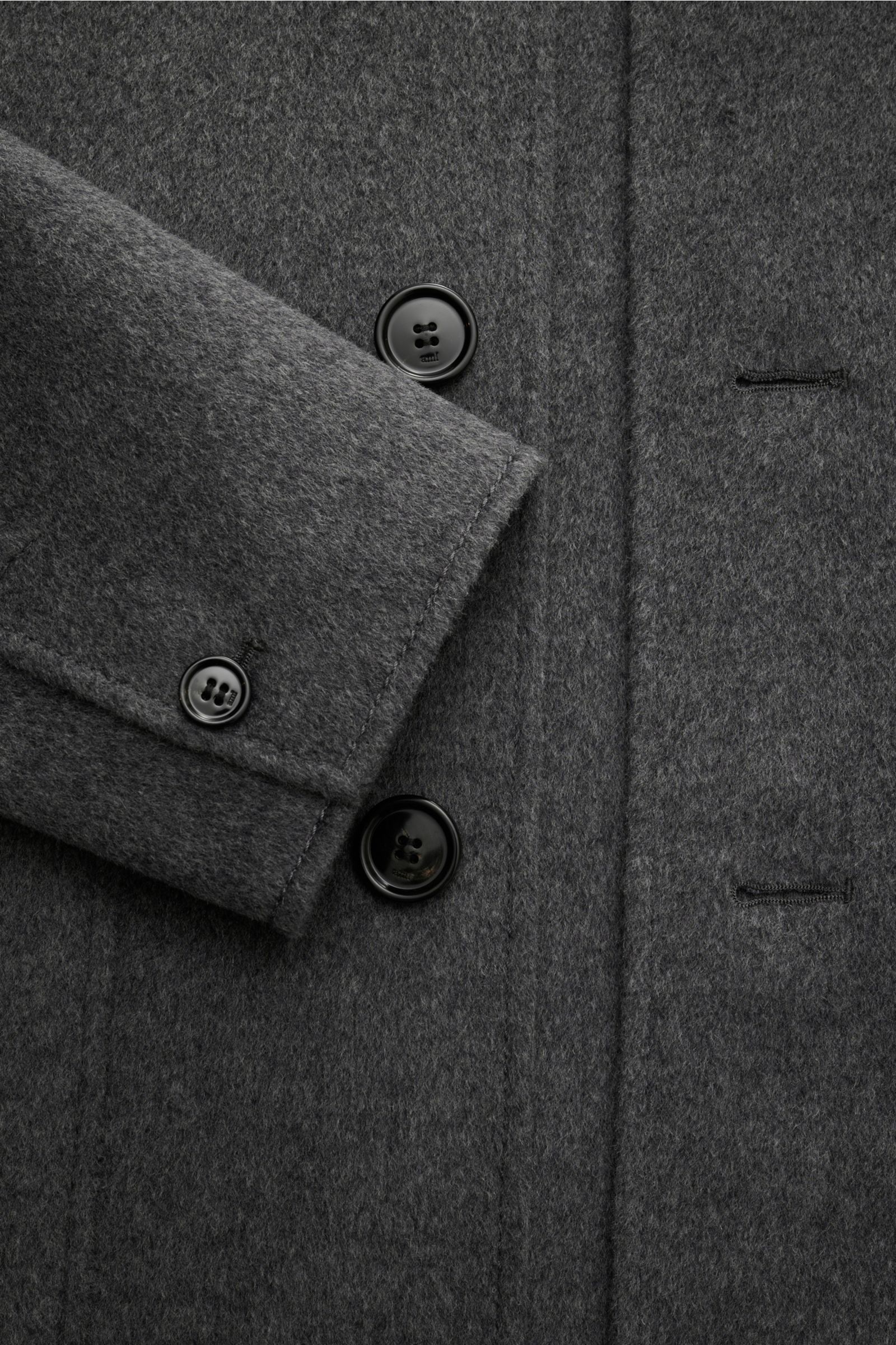 Nahaufnahme der Ami Paris Jacke grau meliert aus schräger Vogelperspektive, Slim Fit mit Schurwolle und Cashmere, weicher Griff, fünf-Knopf-Leiste, Umlegekragen, aufgesetzte Fronttaschen, Ärmelabschlüsse mit Knopf, rückwärtige Logo-Prägung, ungefüttert, e