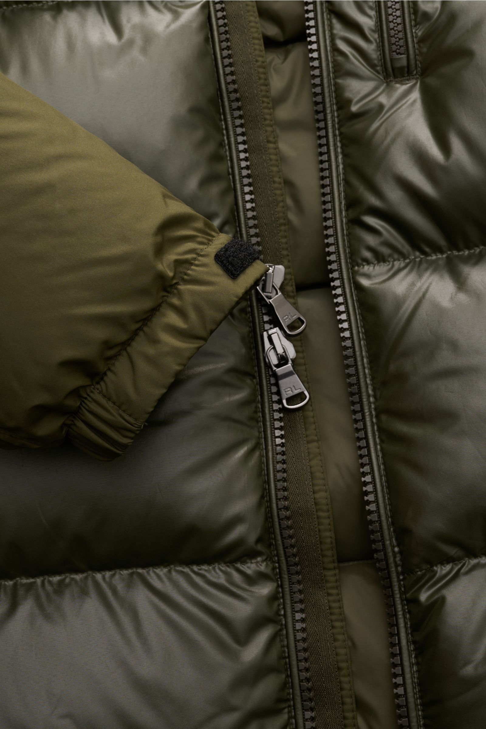 Close-up front view of Polo Ralph Lauren Daunenjacke oliv with shiny olive fabric, dual zipper, elastic cuff, and padded down filling.

Setzen Sie ein Statement - auch im Winter: Diese Daunenjacke von POLO RALPH LAUREN wärmt dank ihrer Daunenfüllung ga