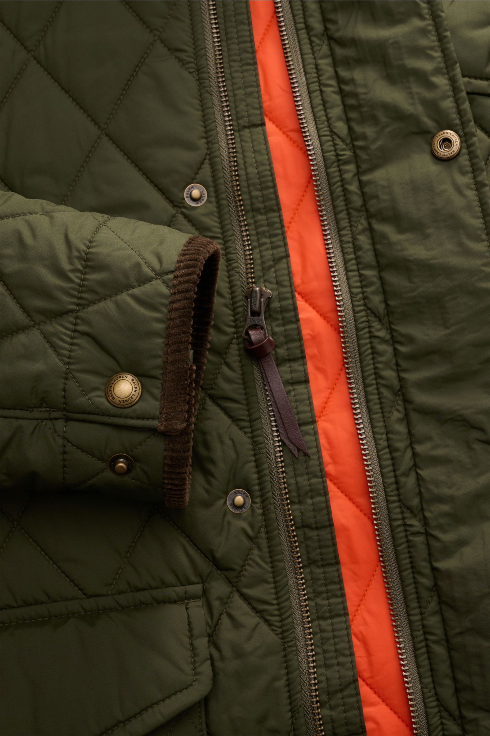 Nahaufnahme der Polo Ralph Lauren Steppjacke 'Beaton' oliv in Retro-Optik, zeigt Reißverschluss, Cordbesatz am Ärmel und orangefarbenes Innenfutter.