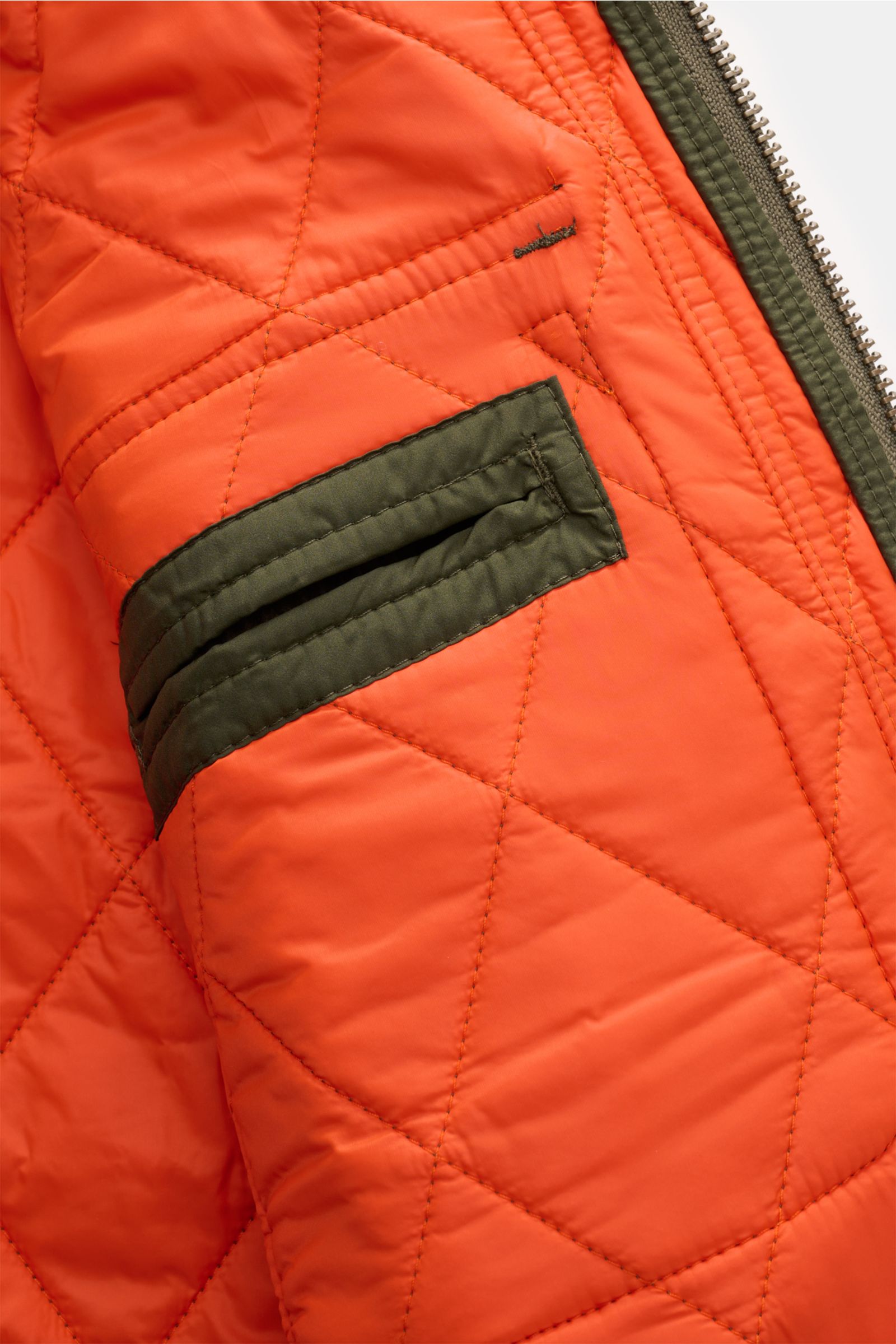 Nahaufnahme der Innenseite der Polo Ralph Lauren Steppjacke 'Beaton' oliv mit orangefarbenem, gestepptem Futter, grüner Innentasche und Reißverschluss.