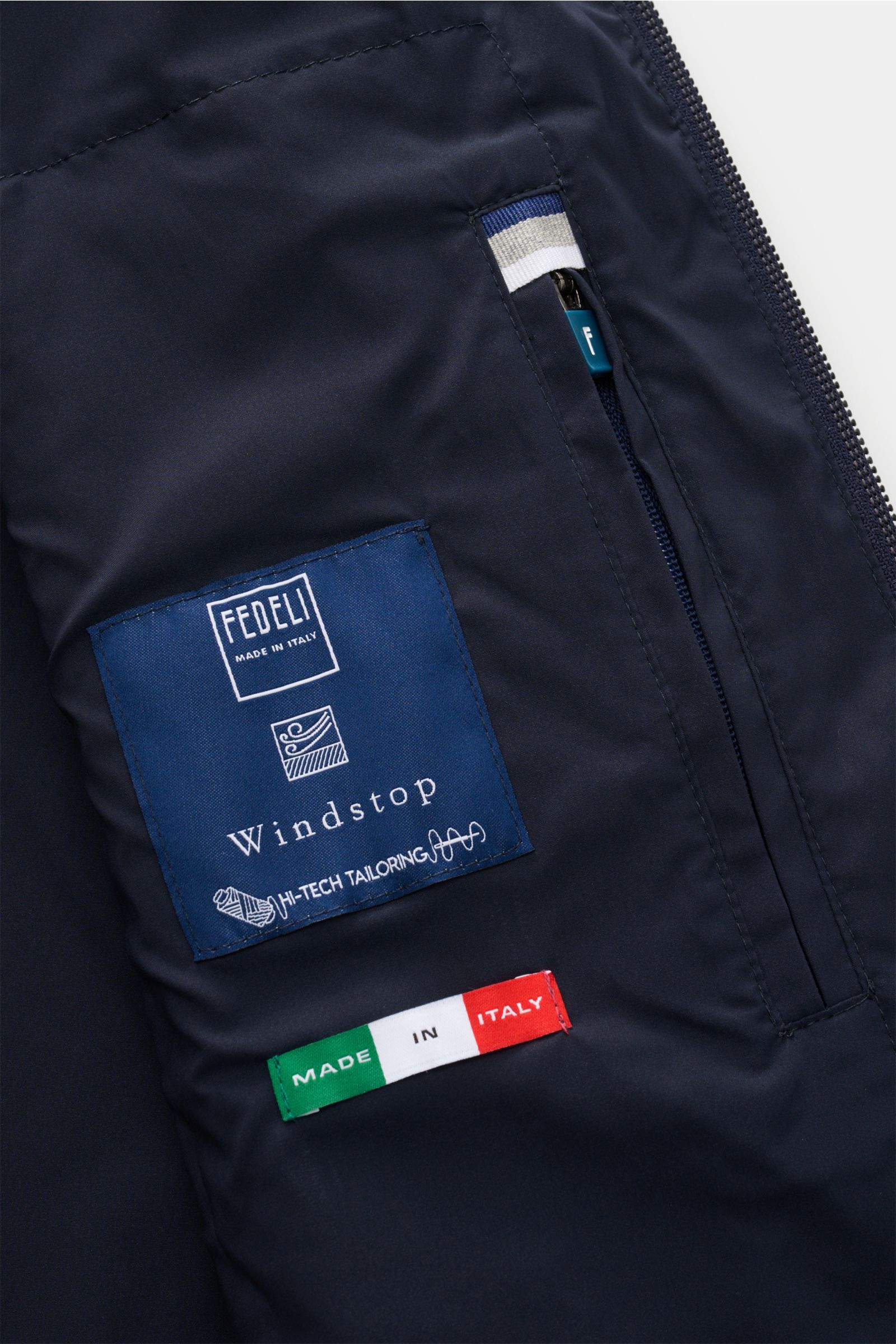 Close-up inside view of Fedeli Windbreaker Blouson 'Paros' navy showing blue brand label, Made in Italy tag, and zippered inner pocket.

Zwei Fabrics - ein Anspruch: Der Blouson 'Paros' von FEDELI vereint feinen Strick aus reiner Super 140'S Wolle mit 