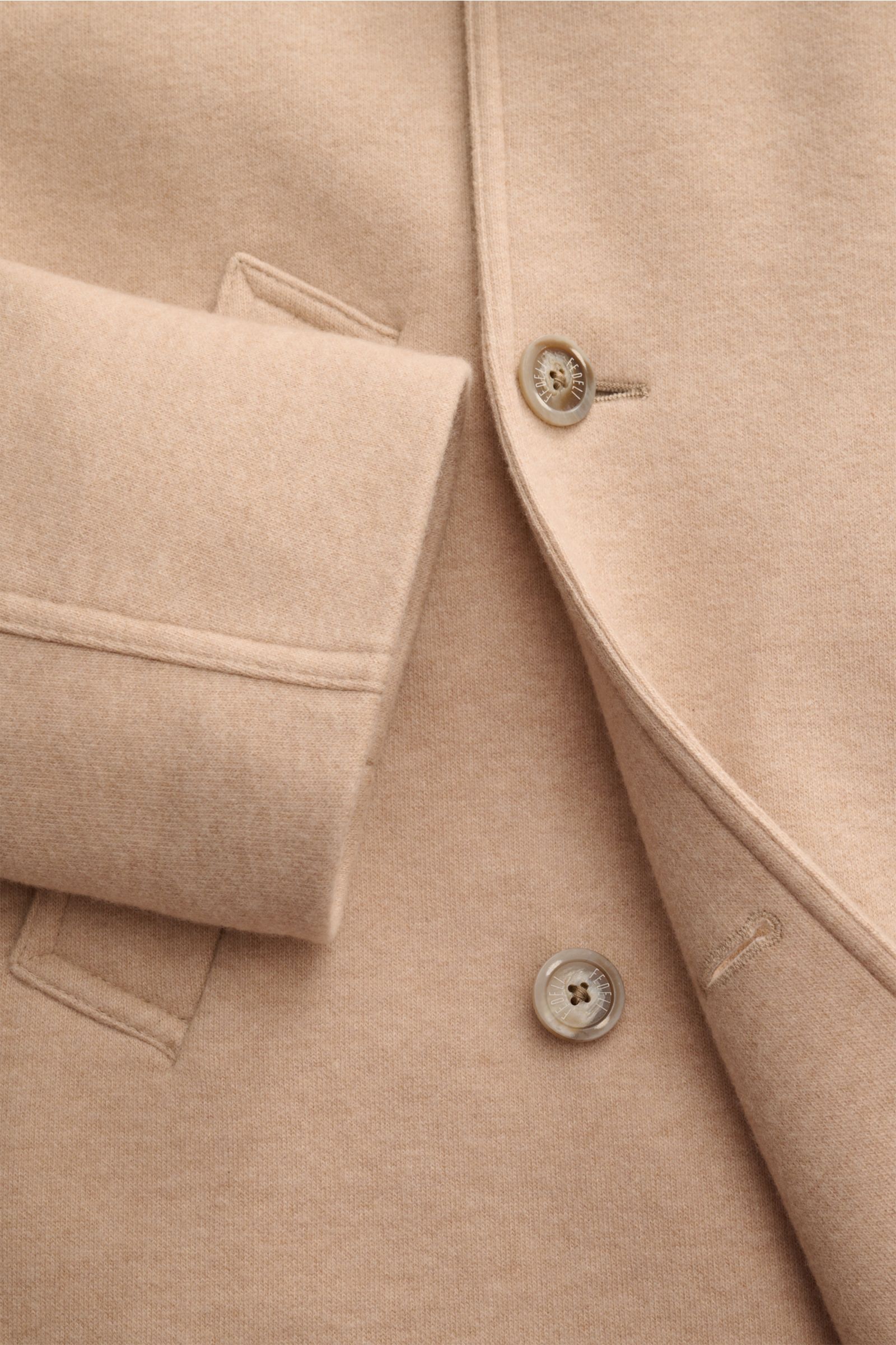 Close-up front view of the Fedeli Cashmere Cabanjacke beige showing reiner Cashmere, weicher, geschmeidiger Griff, Slim Fit, variabler Kragen, Vier-Knopf-Leiste, schräge Leistentaschen, halb gefüttert, and zwei Innentaschen.