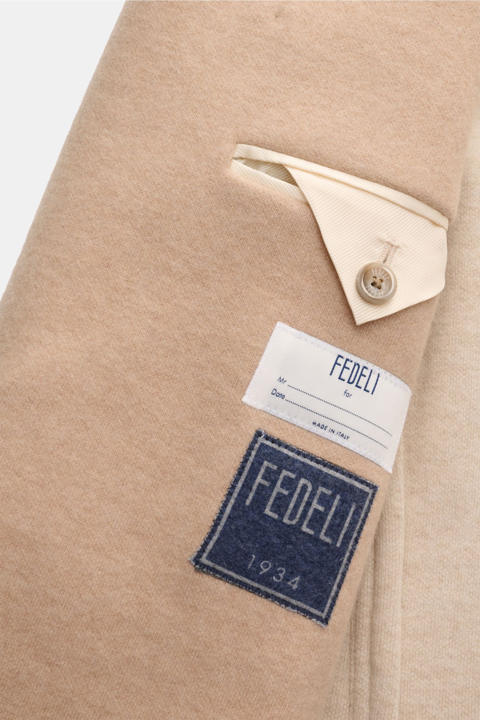 Close-up view of the beige Fedeli Cashmere Cabanjacke showing the soft cashmere fabric, slanted welt pocket with button flap, and Fedeli labels, highlighting reiner Cashmere, weicher, geschmeidiger Griff, Slim Fit, variabler Kragen, Vier-Knopf-Leiste, sch