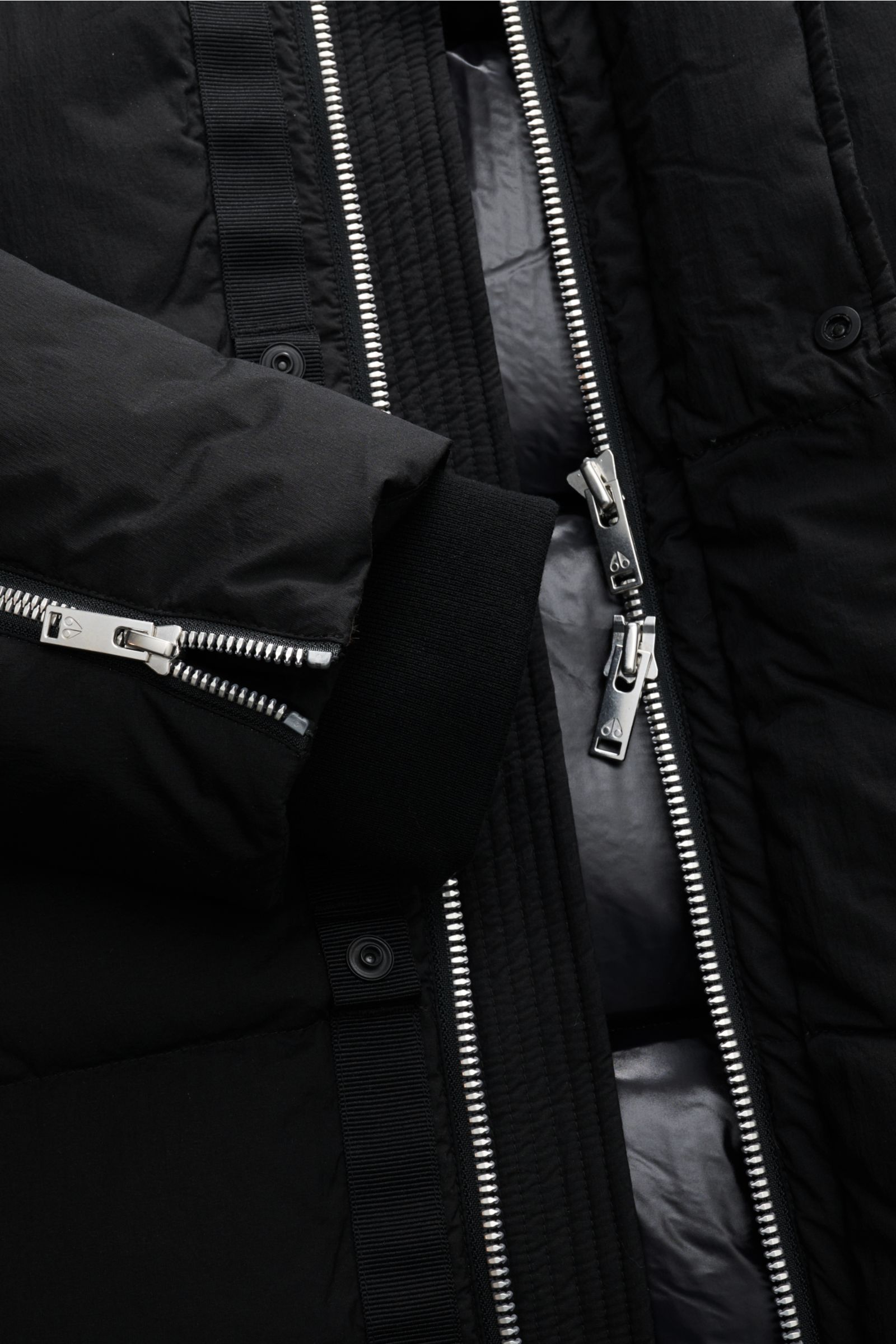 Close-up front view of Moose Knuckles Daunenjacke 'Everest 3Q' schwarz showing silver two-way zipper, black cuff with zipper, and inner shiny lining.

Höchster Komfort bei jeder Temperatur: Die Daunenjacke von MOOSE KNUCKLES vereint exzellente Wärmeiso