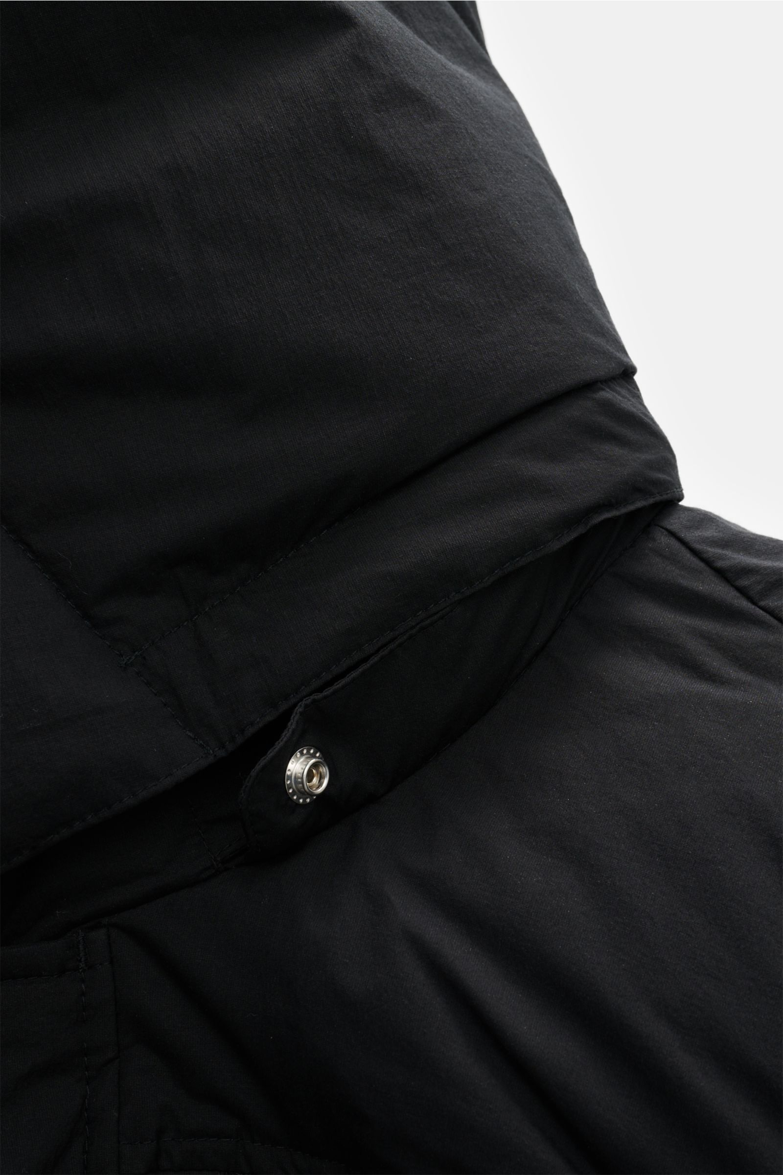 Close-up view of the collar and upper shoulder area of the Moose Knuckles Daunenjacke 'Everest 3Q' schwarz, showcasing its matte black cotton and microfiber fabric with a wind- and water-repellent finish and a metal snap button detail. Höchster Komfort be