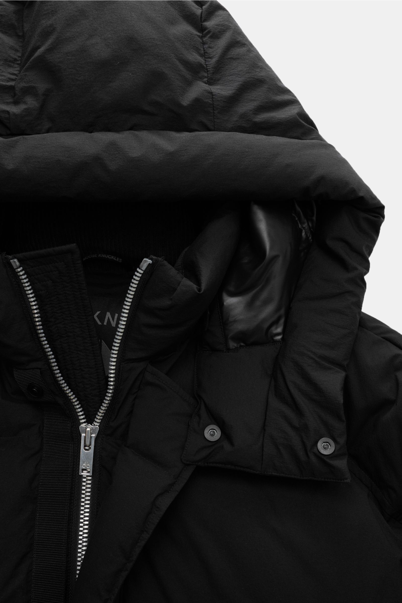 Nahaufnahme des schwarzen Moose Knuckles Daunenmantel 'Everest Long Puffer' von schräg oben, zeigt Kapuze, Reißverschluss und windabweisende Microfaser.