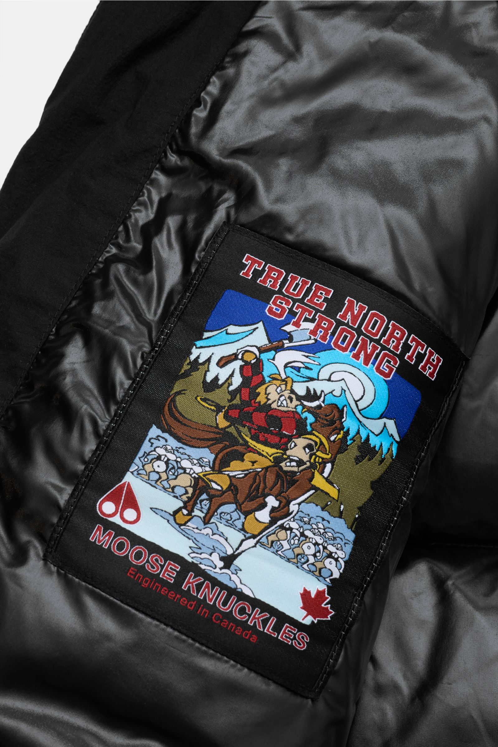 Nahaufnahme des Innenfutters mit Label des Moose Knuckles Daunenmantel 'Everest Long Puffer' schwarz, wind- und wasserabweisend, mit Daunenfüllung.