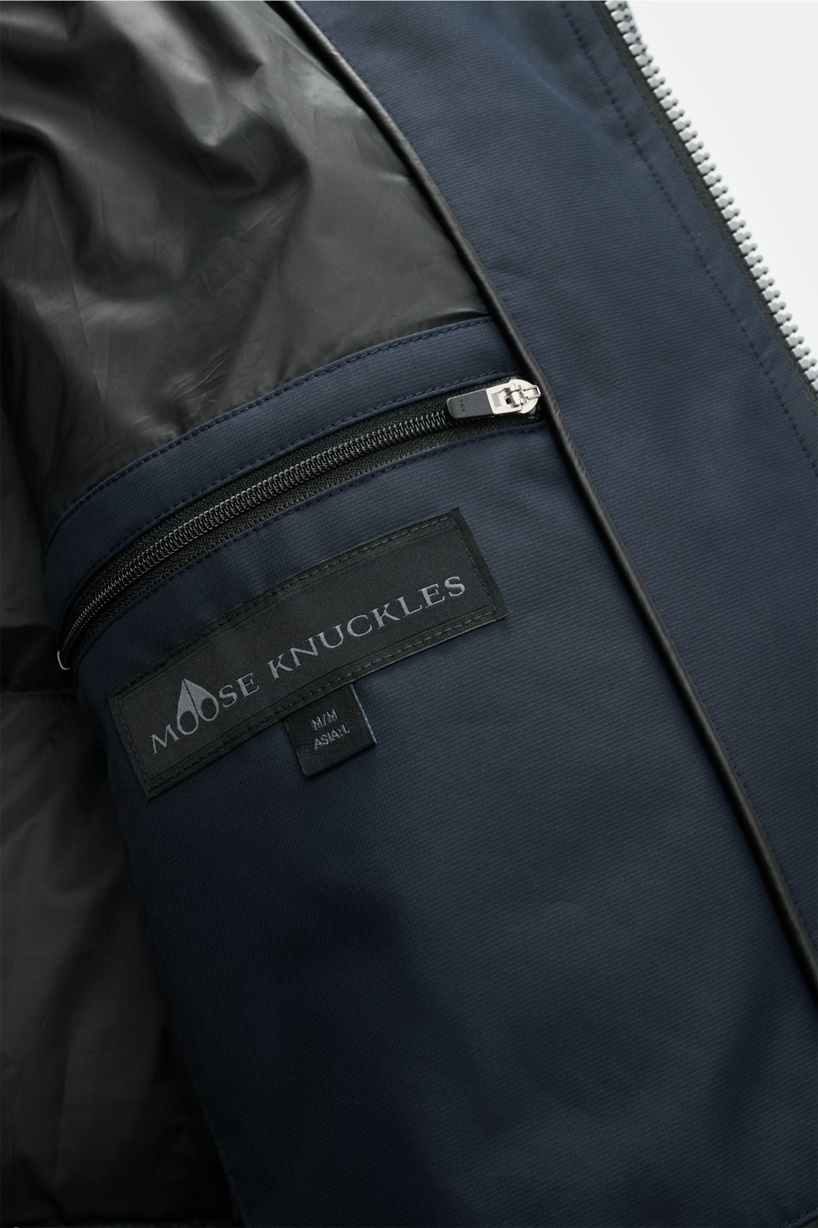 Close-up interior view of the Moose Knuckles Down parka 'Cloud parka Neoshear' navy showing a zippered inside pocket with the Moose Knuckles label on high-quality, smooth, water-repellent microfiber lining.