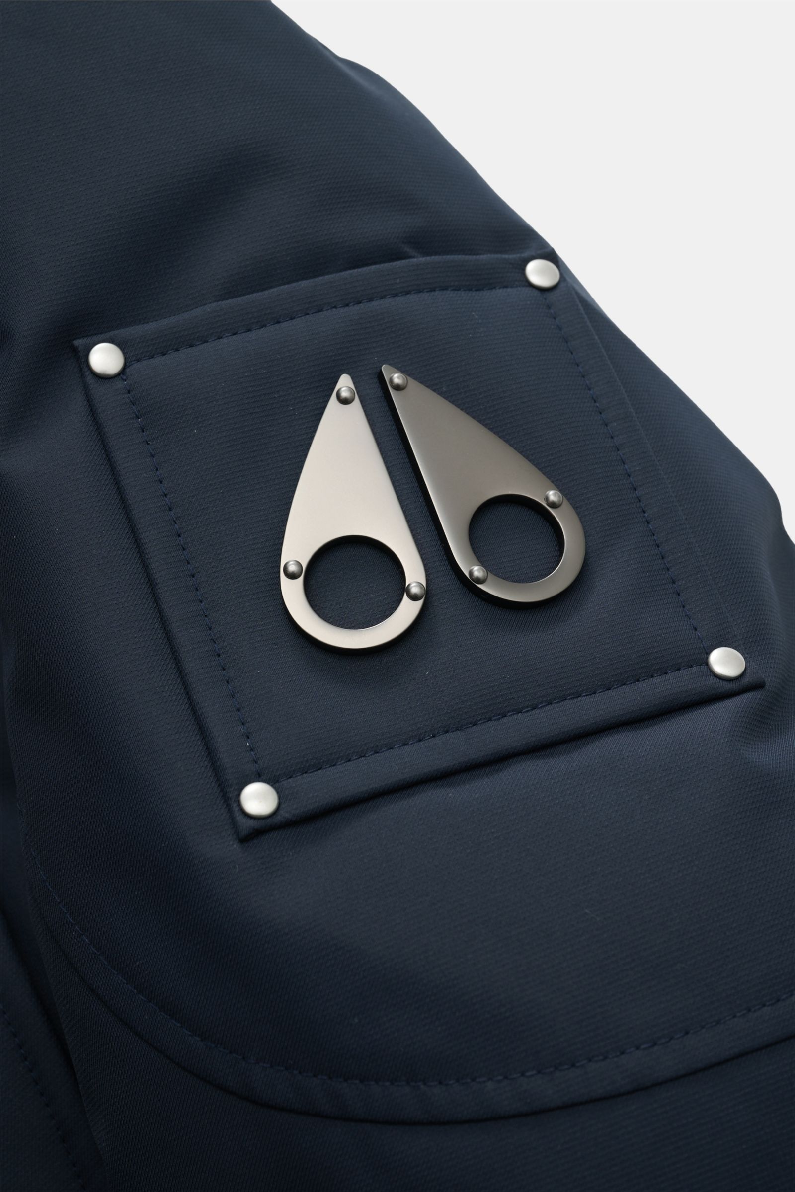 Moose Knuckles Down parka 'Cloud parka Neoshear' navy close-up of upper sleeve logo patch with two metal teardrop shapes on high-quality, water-repellent microfiber. With the 'Cloud' series, MOOSE KNUCKLES presents reinterpretations of its classics that a