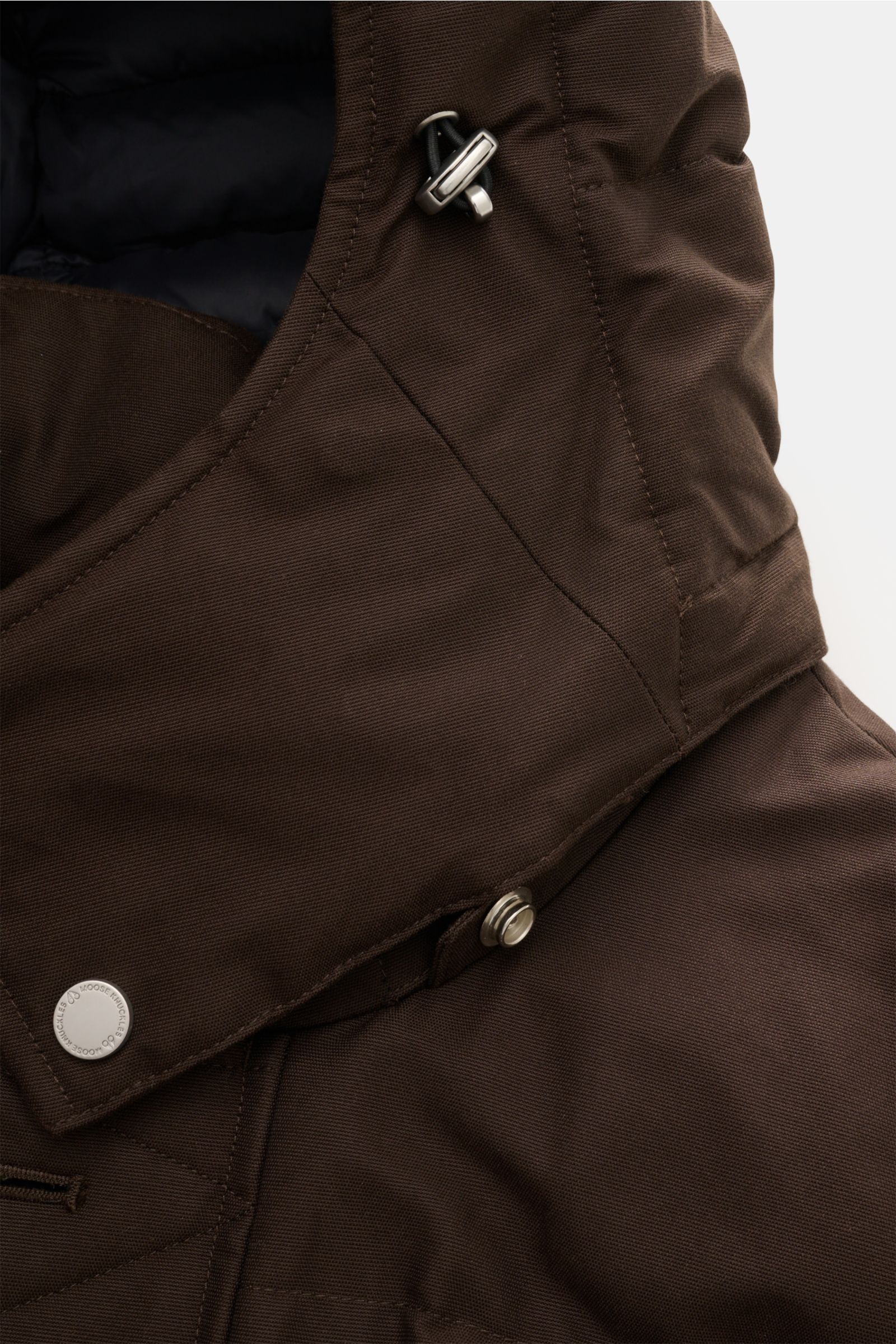 Close-up front angle of the dark brown Moose Knuckles Down jacket 'Original 3q Neoshear' showing fabric texture, detachable hood, and metal logo snap.