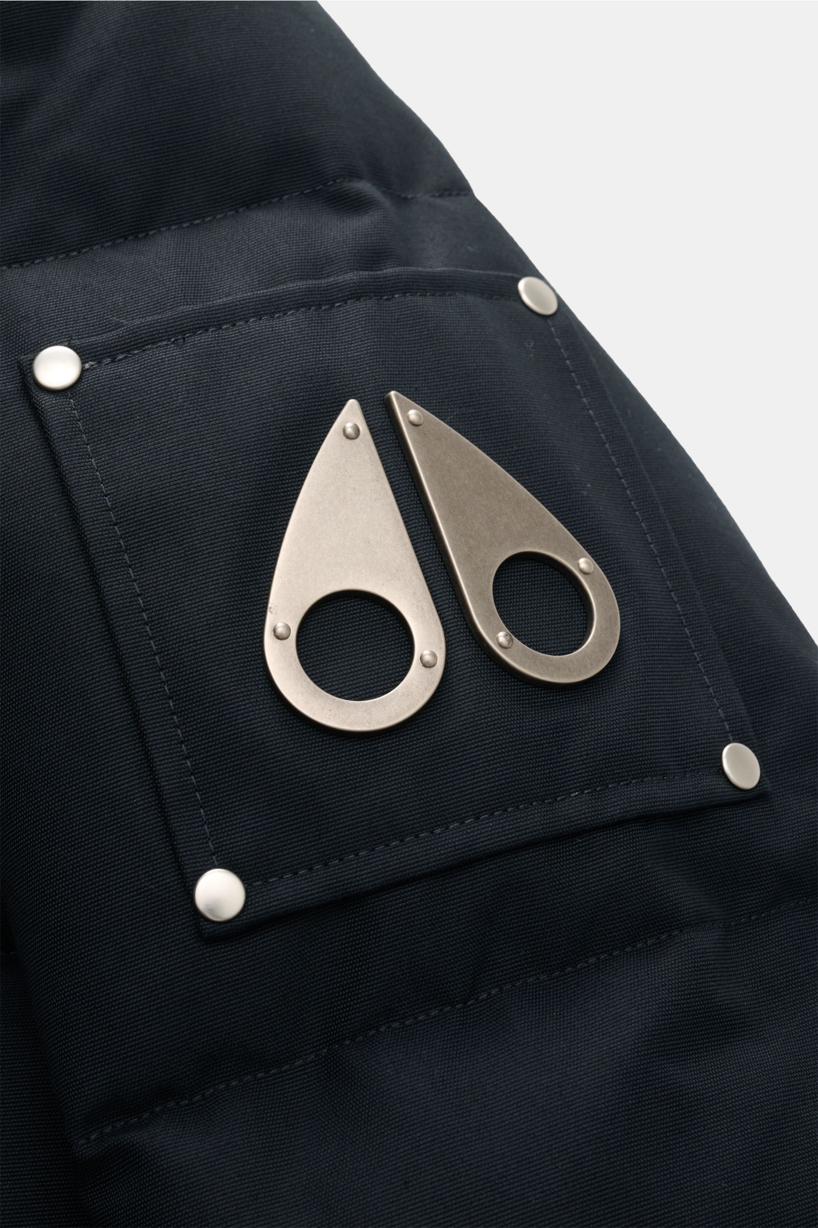 Close-up view of the signature metal logo on the upper sleeve of the Moose Knuckles Down jacket 'Original 3q Neoshear' navy, made from a cotton-microfibre blend with robust, wind- and water-repellent fabric, featuring a warm 90/10 down lining and detachab