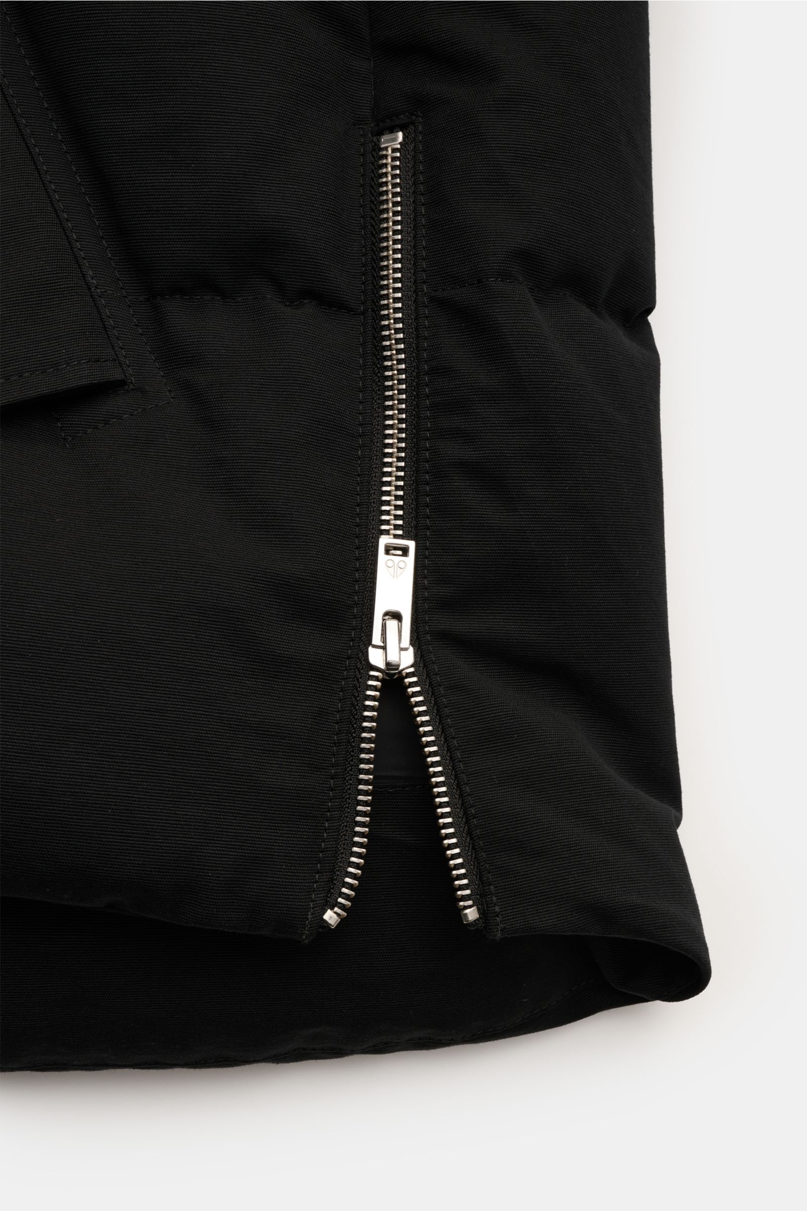 Close-up front view of the lower section of the Moose Knuckles Daunenjacke 'Original 3q Neoshear' schwarz, showing a partially open silver zipper on black, wind- and water-repellent cotton-microfiber fabric with 90/10 down filling for warmth up to -30°C, 