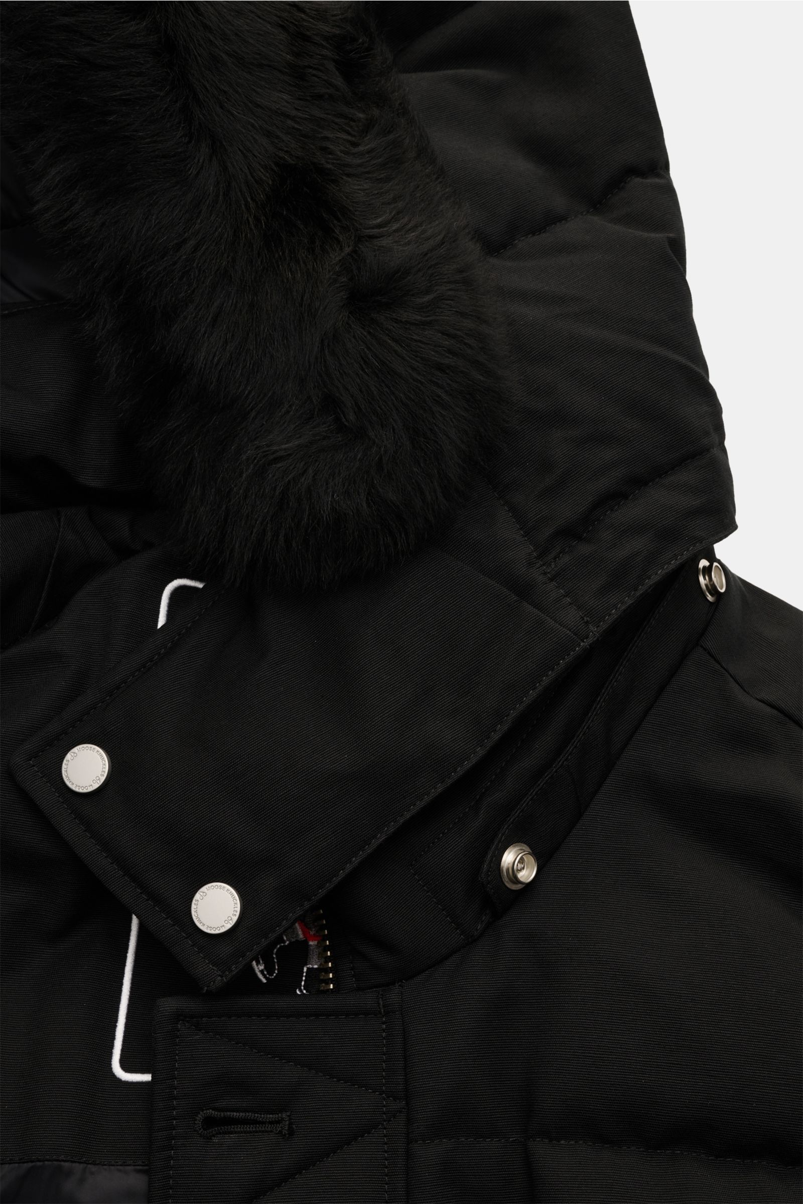 Close-up of the upper front section of the Moose Knuckles Daunenjacke 'Original 3q Neoshear' schwarz, showing the black, wind- and water-resistant cotton-microfiber mix fabric with a detachable fur-trimmed hood and collar, metal snap buttons, and padded 9