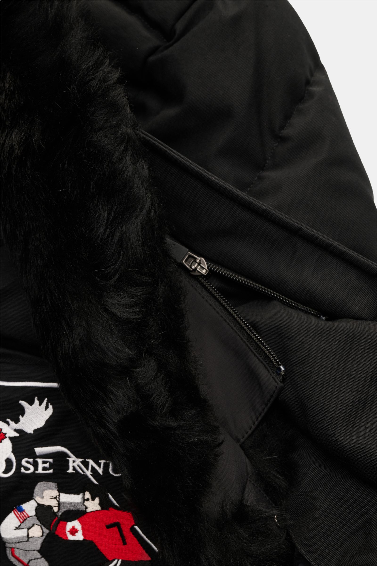 Close-up of the Moose Knuckles Daunenjacke 'Original 3q Neoshear' schwarz showing black fur trim, zipper, and embroidered logo from a top-down angle.