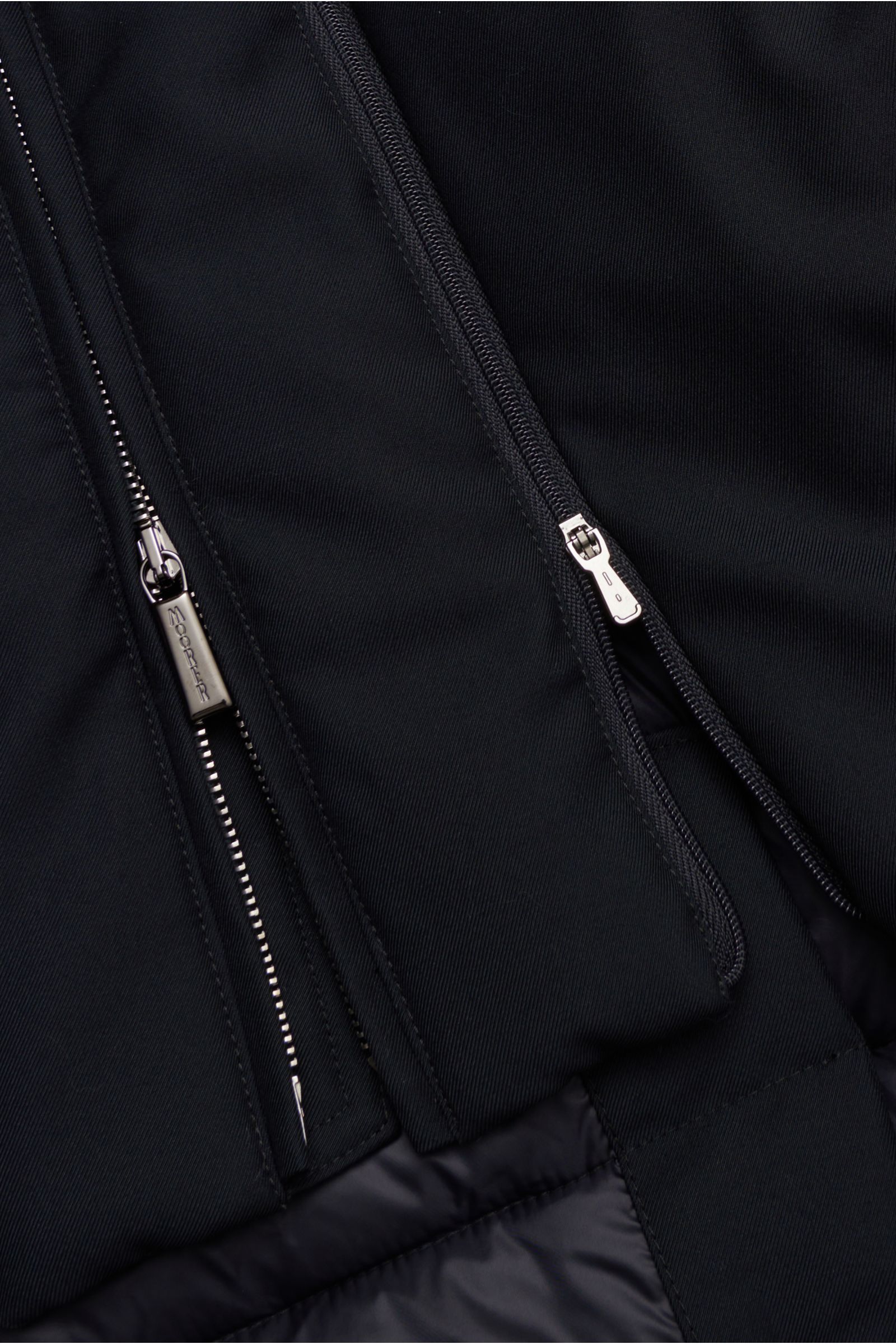 Nahaufnahme aus seitlicher Perspektive der Moorer Daunenjacke 'Imel' dark navy mit funktionaler Microfaser, weichem Griff, wasserabweisend, Slim Fit, wärmender Gänsedaunenfüllung, Stehkragen mit verstaubarer Kapuze, herausnehmbarer Double-Front mit Stehkr
