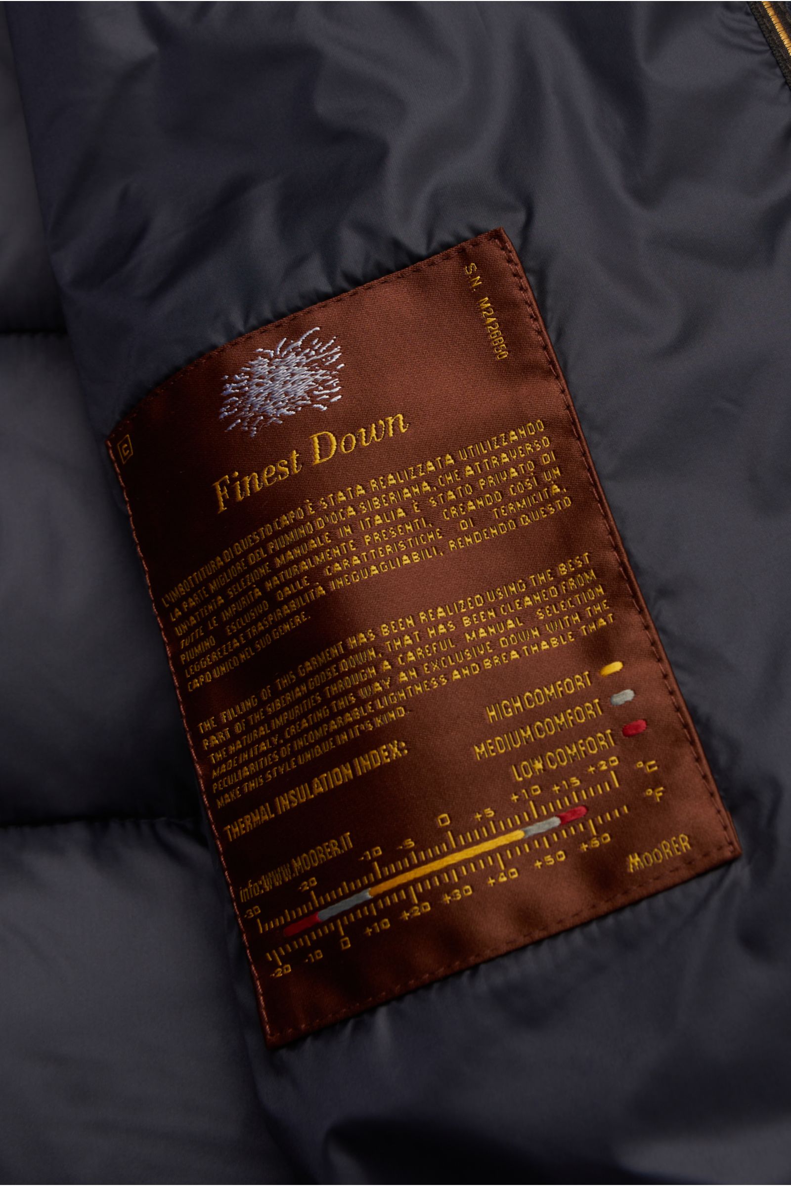 Nahaufnahme des Innenfutters der Moorer Daunenjacke 'Imel' dark navy mit braunem 'Finest Down'-Label, das funktionale Microfaser, weichen Griff, wasserabweisende Oberfläche, wärmende Gänsedaunenfüllung, Slim Fit, Stehkragen mit verstaubarer Kapuze, heraus