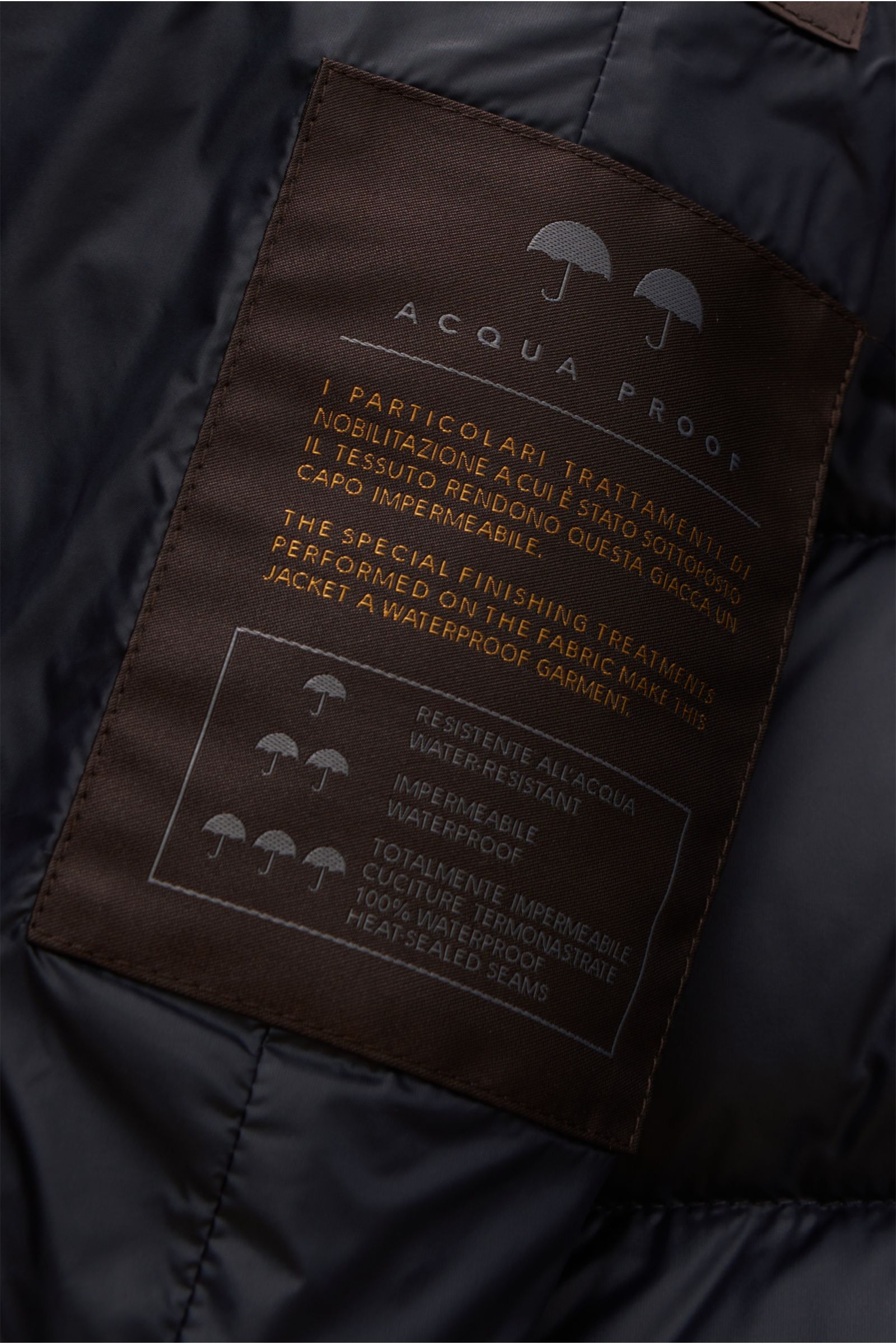 Close-up inside view of the Moorer Daunenjacke 'Ilvo' dark navy showing a brown label with waterproof fabric details, highlighting water-resistant, heat-sealed seams, and special finishing treatments. The waterproof down jacket features a microfibre and v