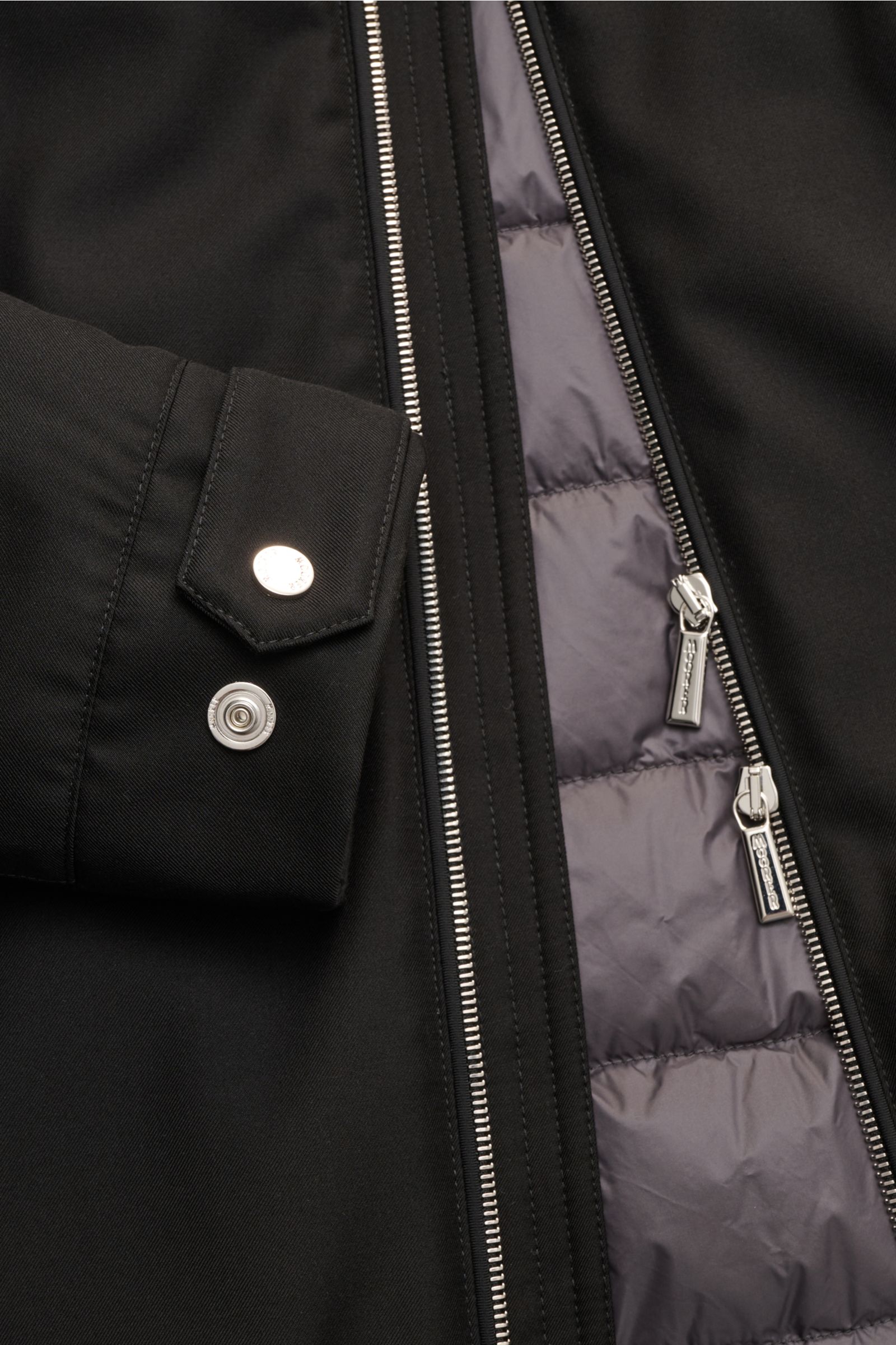Nahaufnahme der Moorer Daunenjacke 'Albini' schwarz von innen mit offenem Zwei-Wege-Reißverschluss, abnehmbarer Kapuze, Daunenfüllung und Knopfriegel am Ärmel.