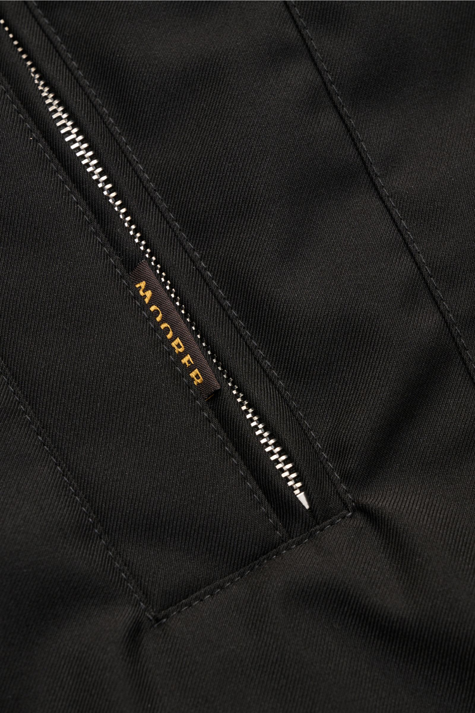 Nahaufnahme der schwarzen Moorer Daunenjacke 'Albini' mit wasserabweisendem Material, Zipper und feiner Steppung, von schräg oben fotografiert.