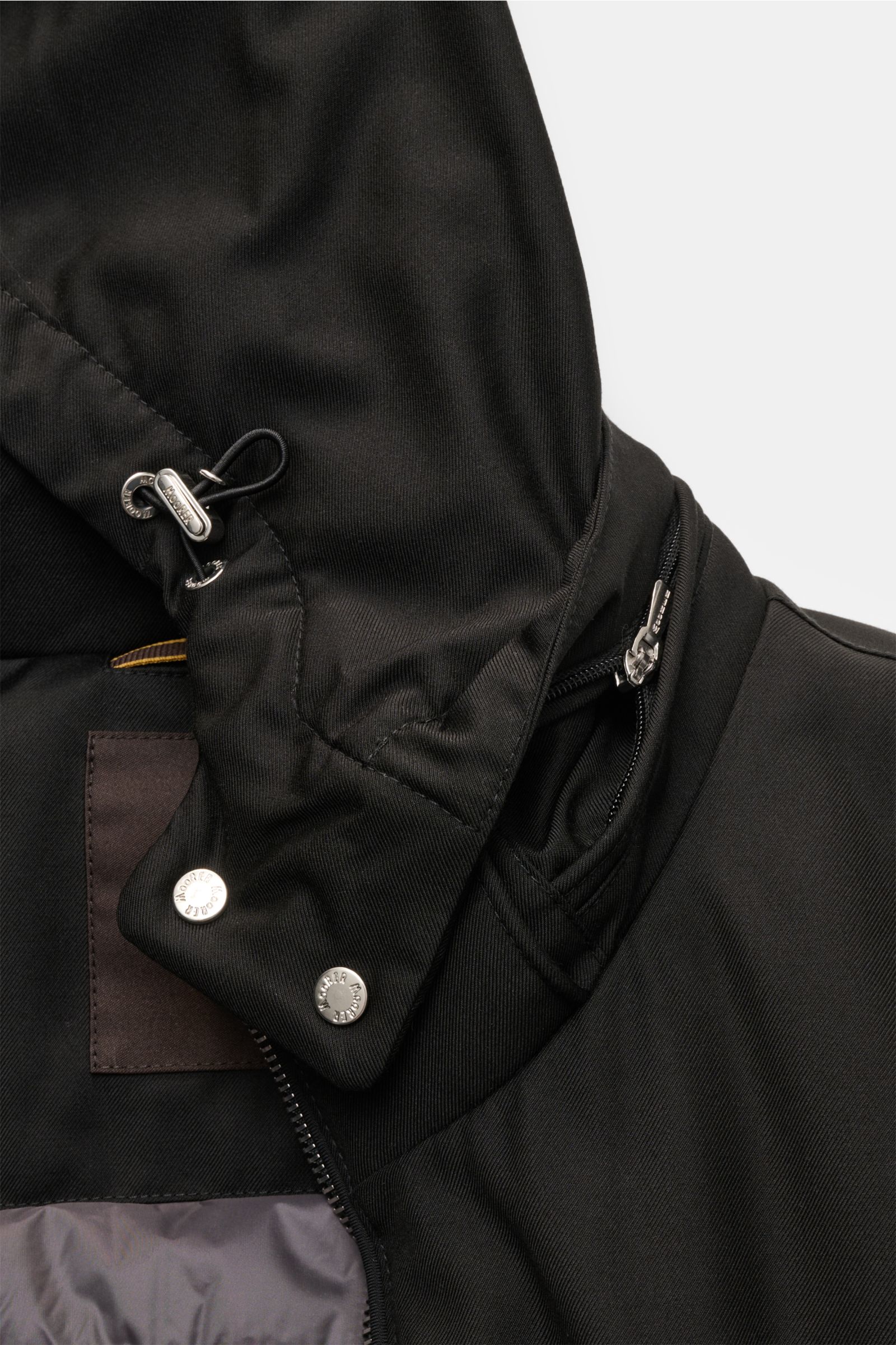 Nahaufnahme der Moorer Daunenjacke 'Albini' schwarz von schräg oben, zeigt abnehmbare Kapuze, wasserabweisendes Material, Slim Fit, Tunnelzug und Reißverschluss.