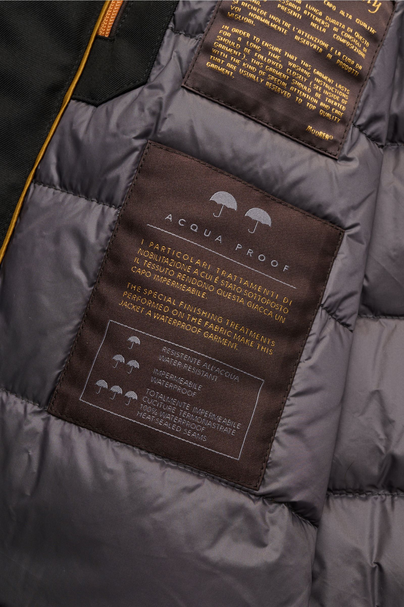 Nahaufnahme des Innenfutters der Moorer Daunenjacke 'Albini' schwarz mit wasserabweisendem, gesteppter Stoff und Pflegeetiketten.