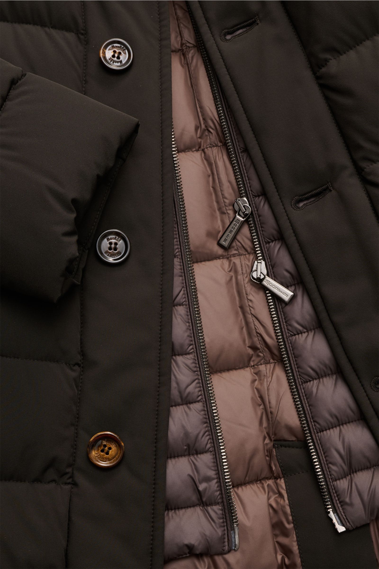 Nahaufnahme der geöffneten Moorer Daunenjacke 'Calegari' graubraun von vorne, zeigt wasserabweisendes Außenmaterial, Gänsedaunenfüllung, Slim Fit und funktionale Details.