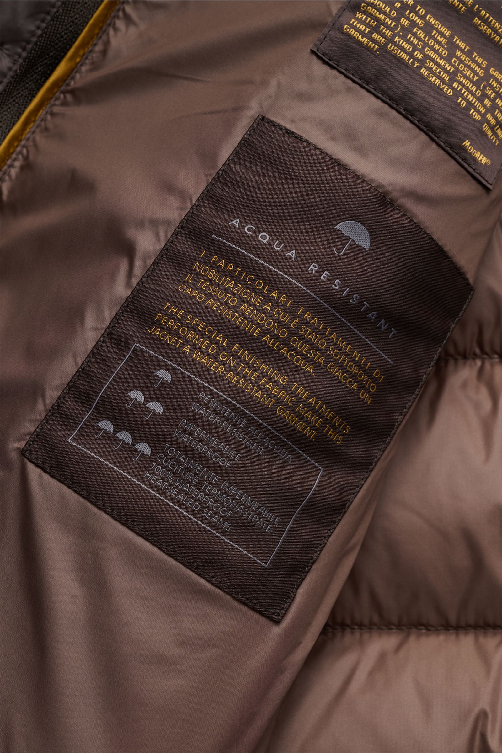 Nahaufnahme des Innenfutters der Moorer Daunenjacke 'Calegari' graubraun mit wasserabweisendem Material, Gänsedaunenfüllung und Etiketten, Frontperspektive.
