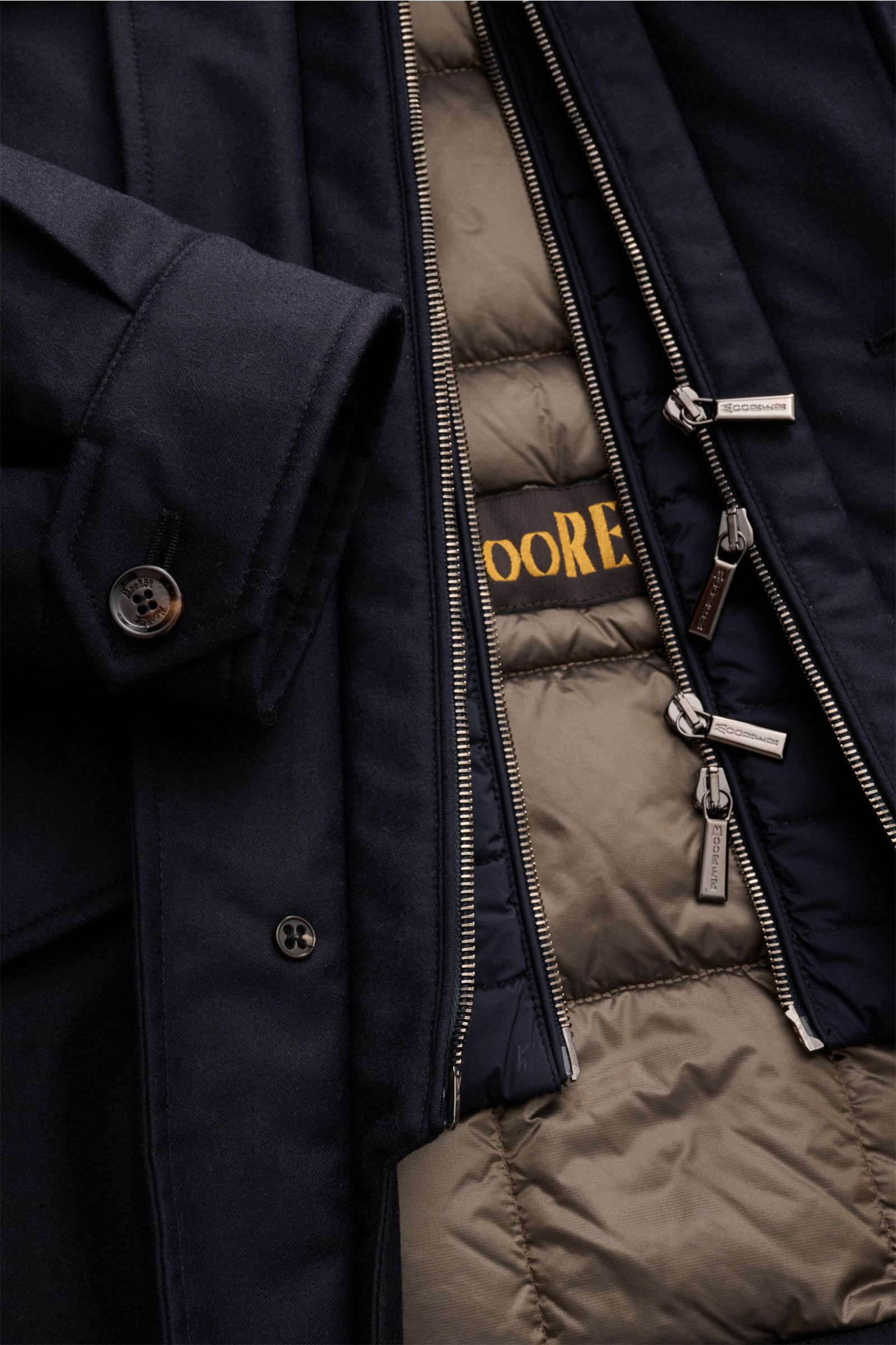Close-up view of the Moorer Daunenjacke 'Isac' navy showing the outer navy wool blend fabric with buttoned cuff and the inner detachable beige down-filled double-front with branded zippers.

Description: Stilvoll durch kalte Tage: Die Jacke 'Isac' von 