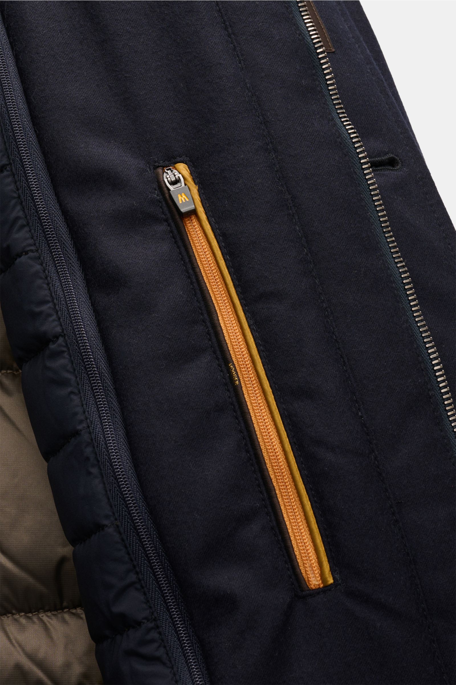 Close-up view of the inside pocket with yellow zipper detail and navy fabric of the Moorer Daunenjacke 'Isac' navy. Stilvoll durch kalte Tage: Die Jacke 'Isac' von MOORER überzeugt mit einem edlen, wasserabweisenden Schurwoll-Mix und einer wärmenden Fü