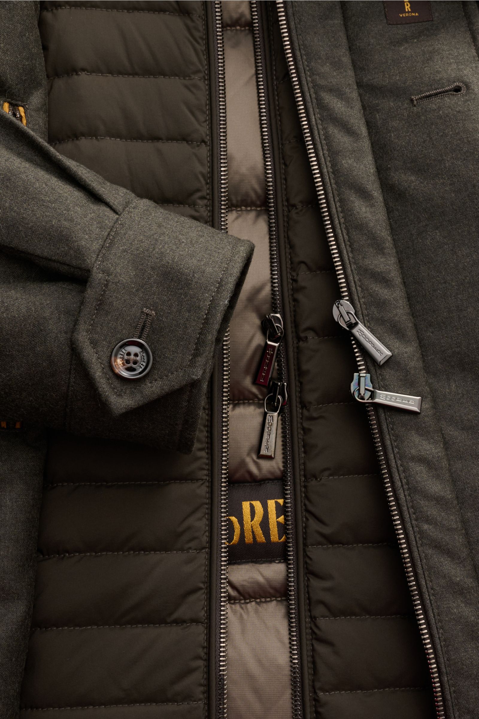 Close-up front view of Moorer Daunenjacke 'Isac' oliv meliert showing water-repellent wool-cashmere blend, goose down filling, removable microfiber double-front, zippers, buttoned cuff, and quilted lining.

Stilvoll durch kalte Tage: Die Jacke 'Isac' v