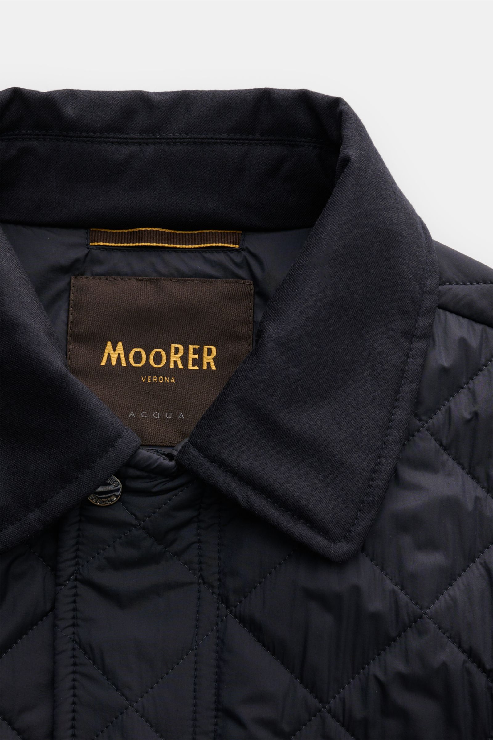 Close-up front view of the Moorer Daunenjacke 'Zavyer' dark navy showing the quilted fabric, soft cotton collar, and brand label. Stilvoll durch die kühle Jahreszeit wird Sie die edle Steppjacke 'Zavyer' von MOORER begleiten, die dank leichter Daunenfü
