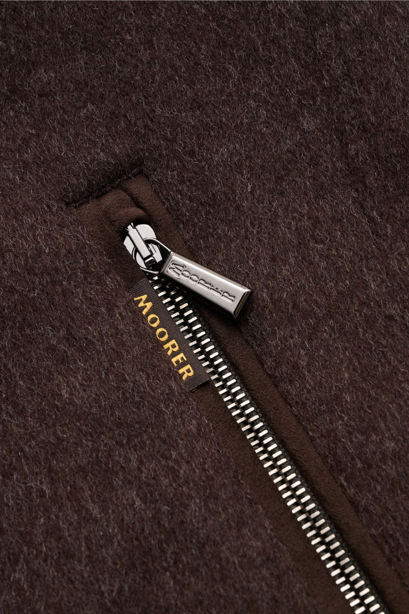 Nahaufnahme des Reißverschlusses am Moorer Daunenblouson 'Bellati' dunkelbraun mit Woll-Cashmere-Mix, gestrickter Außenseite und Zipper-Fronttaschen.