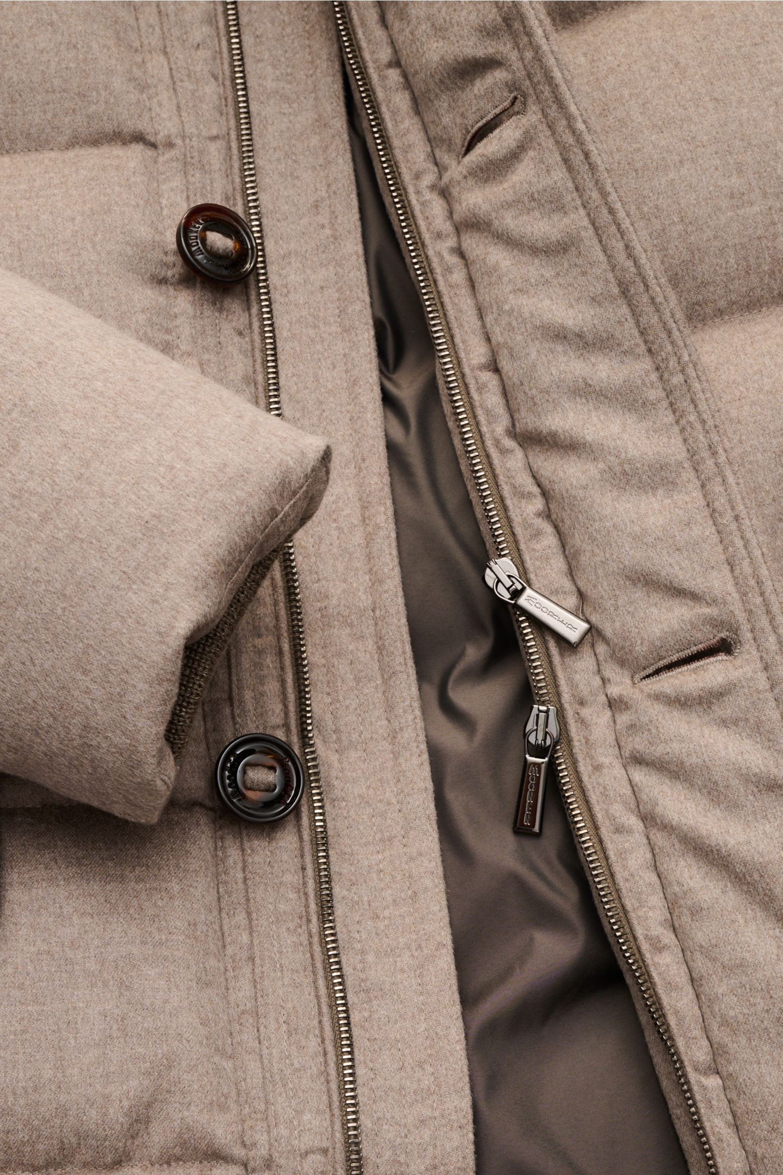 Nahaufnahme des taupefarbenen Moorer Cashmere Daunenparka 'Gorner' mit offenem Zwei-Wege-Reißverschluss und Knöpfen, weicher Cashmere-Stoff.
