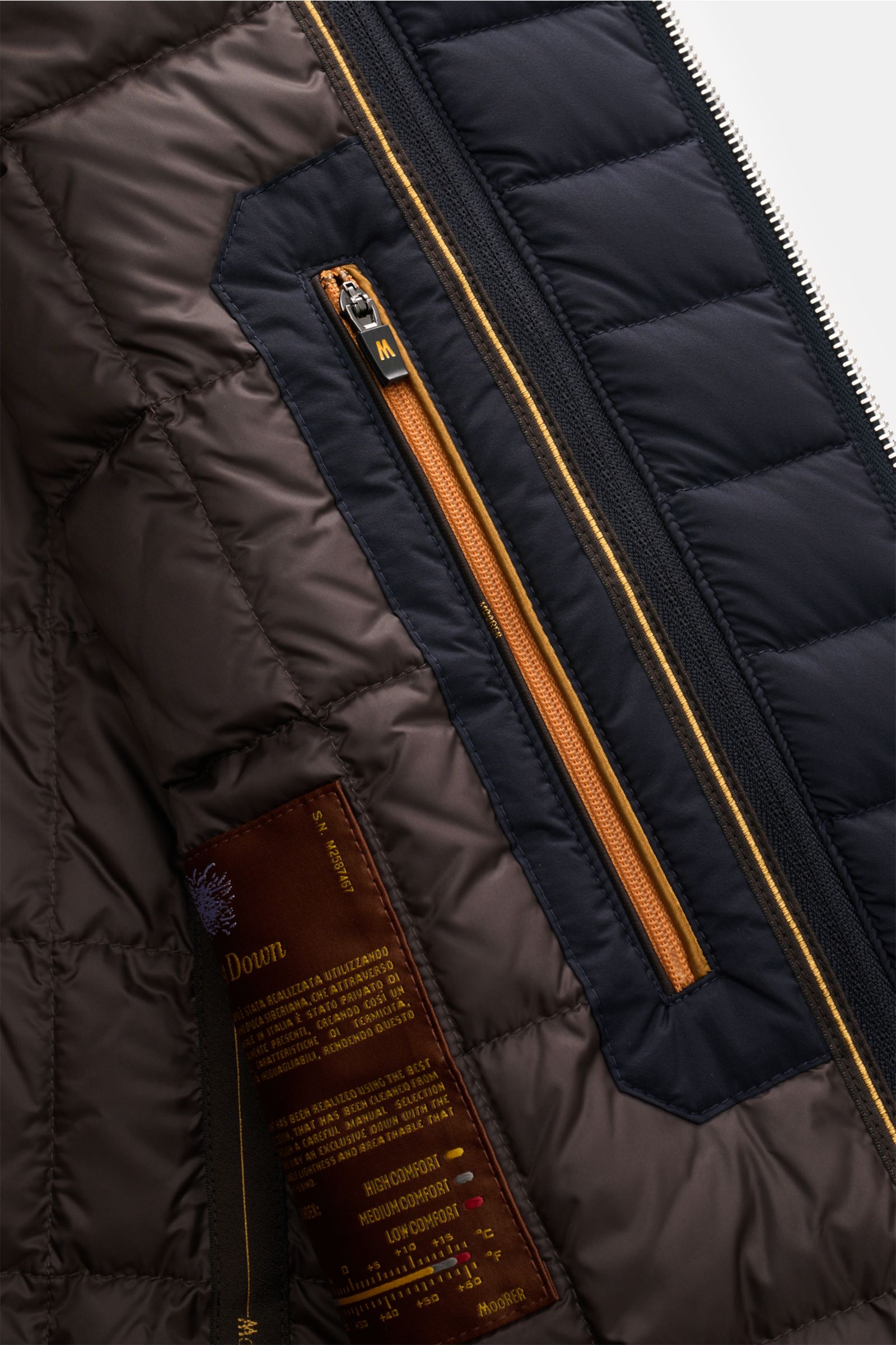 Close-up inside view of the Moorer Cashmere Daunenjacke 'Mendel' navy showing quilted brown lining, orange zippered inner pocket, and stitched details. Understated luxury with pure cashmere, soft touch, removable double-front, warm down filling, slim fit,