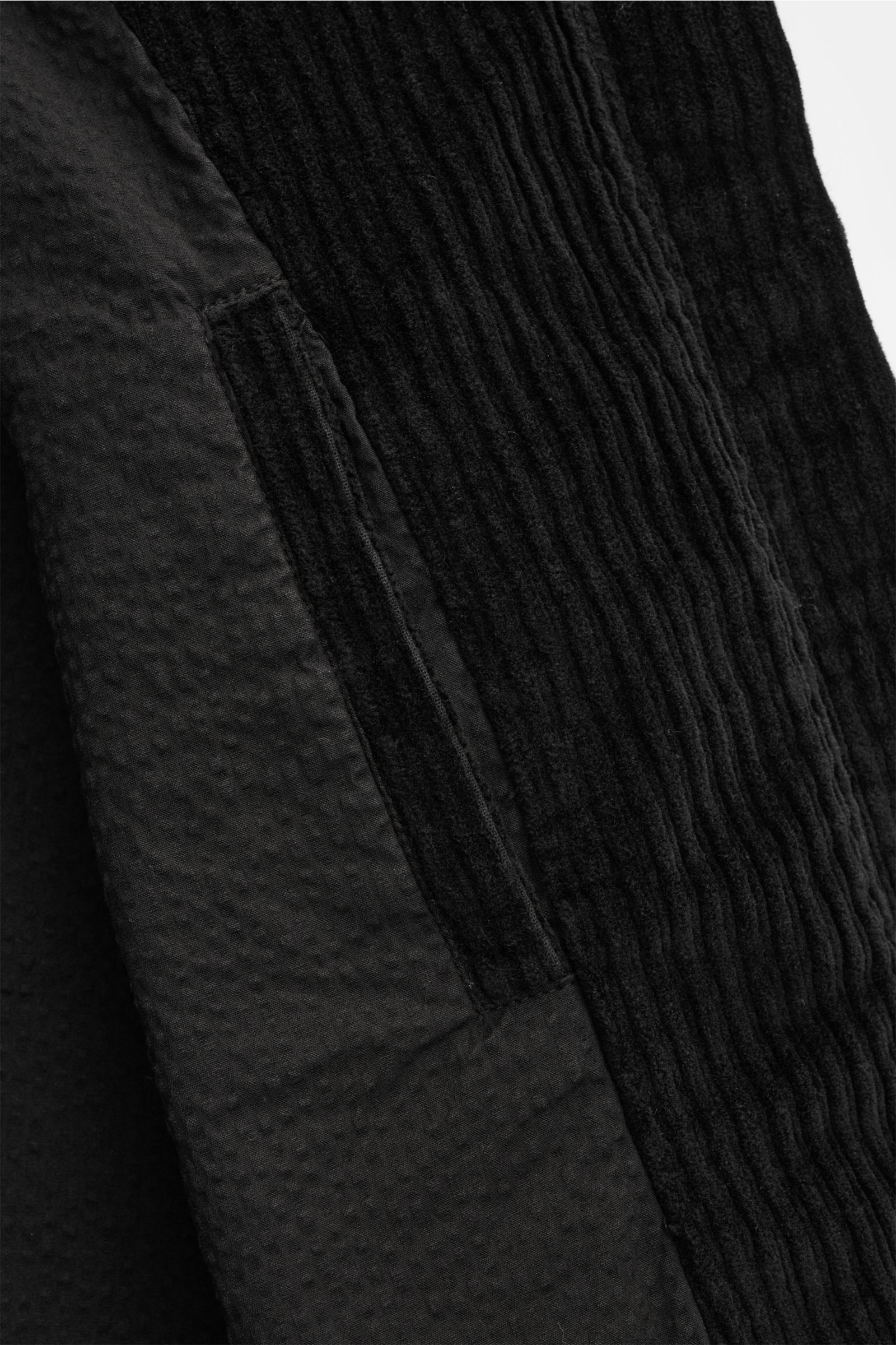 Nahaufnahme der schwarzen 04651/ A trip in a bag Cordjacke, seitlich fotografiert, zeigt paspelierte Fronttasche, elastische Baumwolle und weichen Griff.