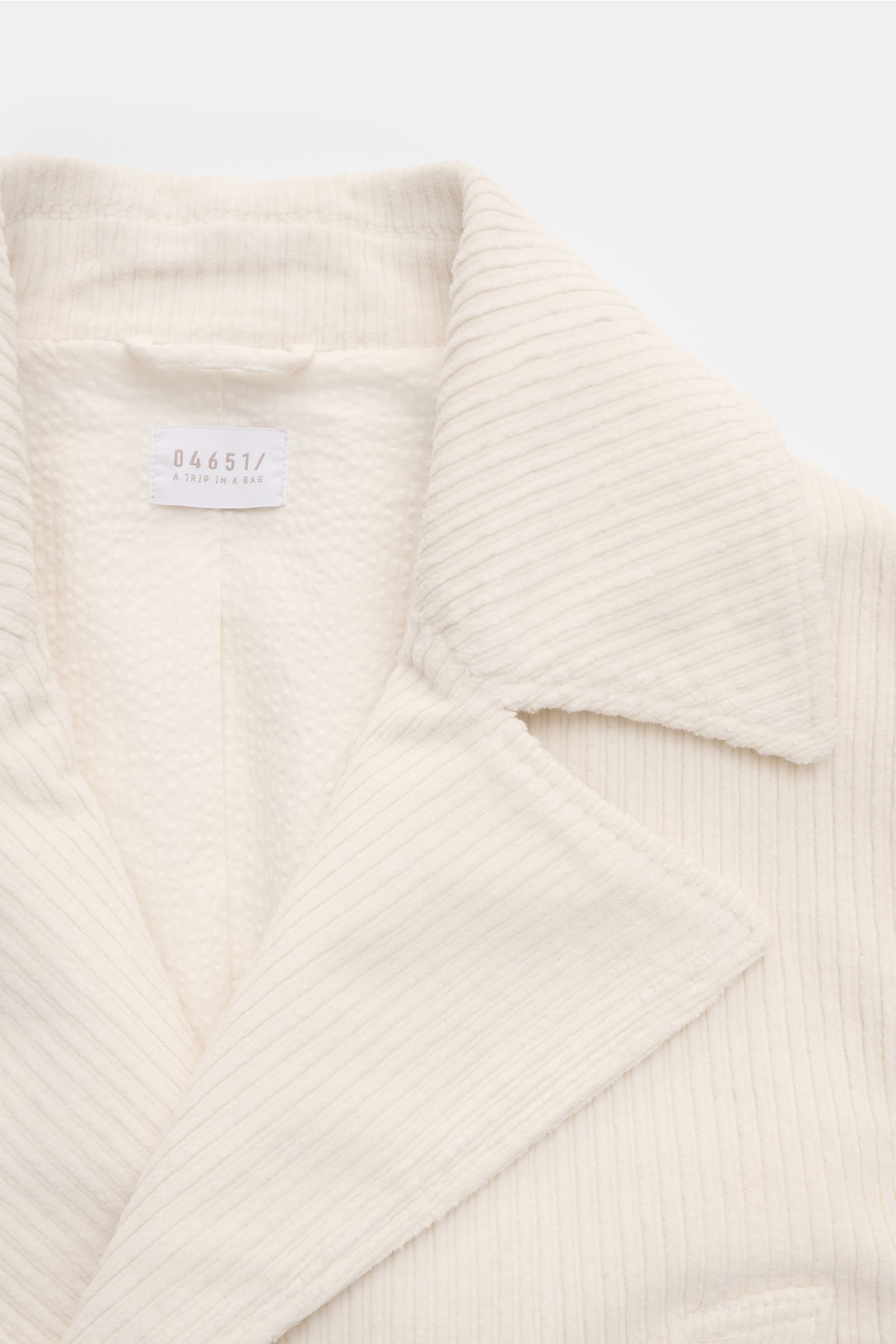 Nahaufnahme der cremefarbenen 04651/ A trip in a bag Cord-Cabanjacke mit voluminösem Breitcord und Seersucker-Futter, Detail vom Reverskragen.