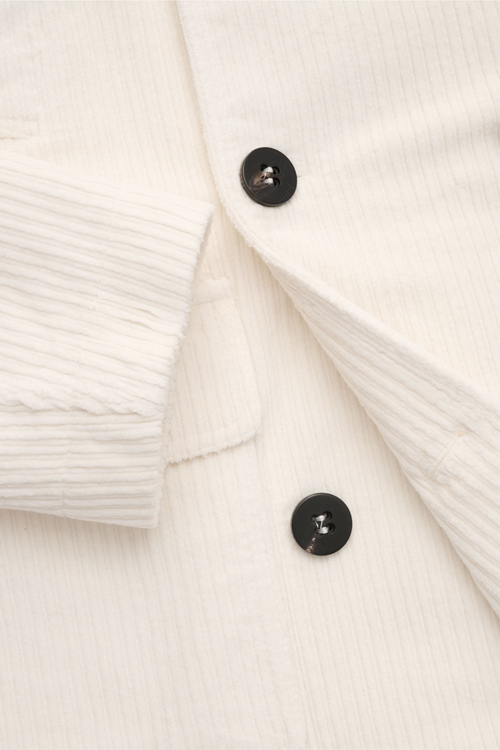 Nahaufnahme aus schräger Perspektive der cremefarbenen 04651/ A trip in a bag Cord-Cabanjacke mit voluminösem Breitcord, schwarzer Knopfleiste und Manschette.