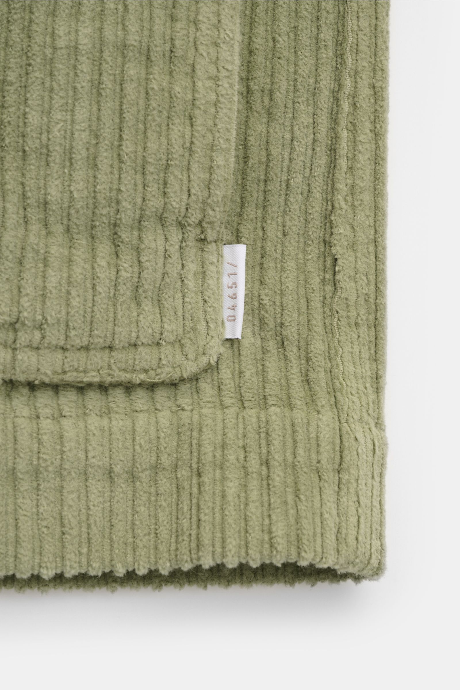 Nahaufnahme der salbeigrünen 04651/ A trip in a bag Cord-Cabanjacke mit voluminösem Breitcord und sichtbarem Weblabel, Frontdetail.