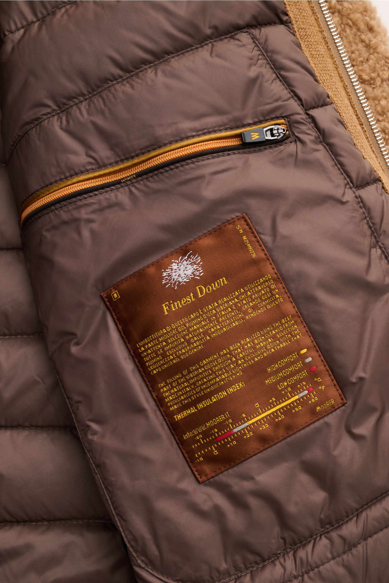 Innenansicht des Moorer Daunenblouson 'Arena' camel mit gestepptem Futter, Reißverschluss-Innentasche und Label 'Finest Down' aus Seide-Kamelhaar.