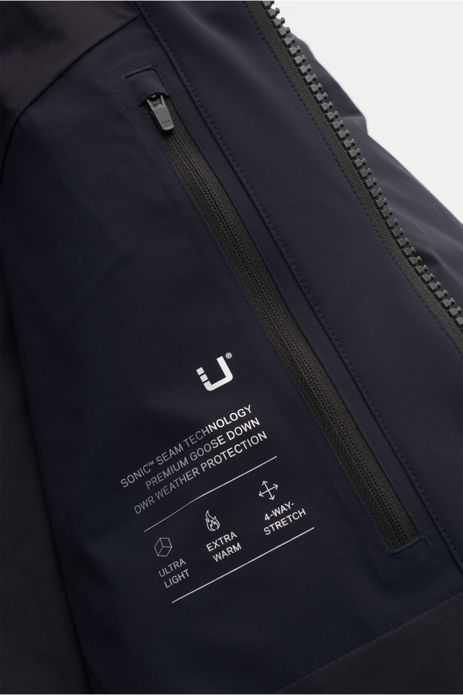 Nahaufnahme der UBR Daunenjacke 'Titan' dark navy von vorne rechts, zeigt Reißverschluss, Logo-Print und technische Microfaser, wasserdicht, atmungsaktiv, mit Gänsedaunenfüllung, regular fit, reflektierendem Logo und mehreren Taschen.