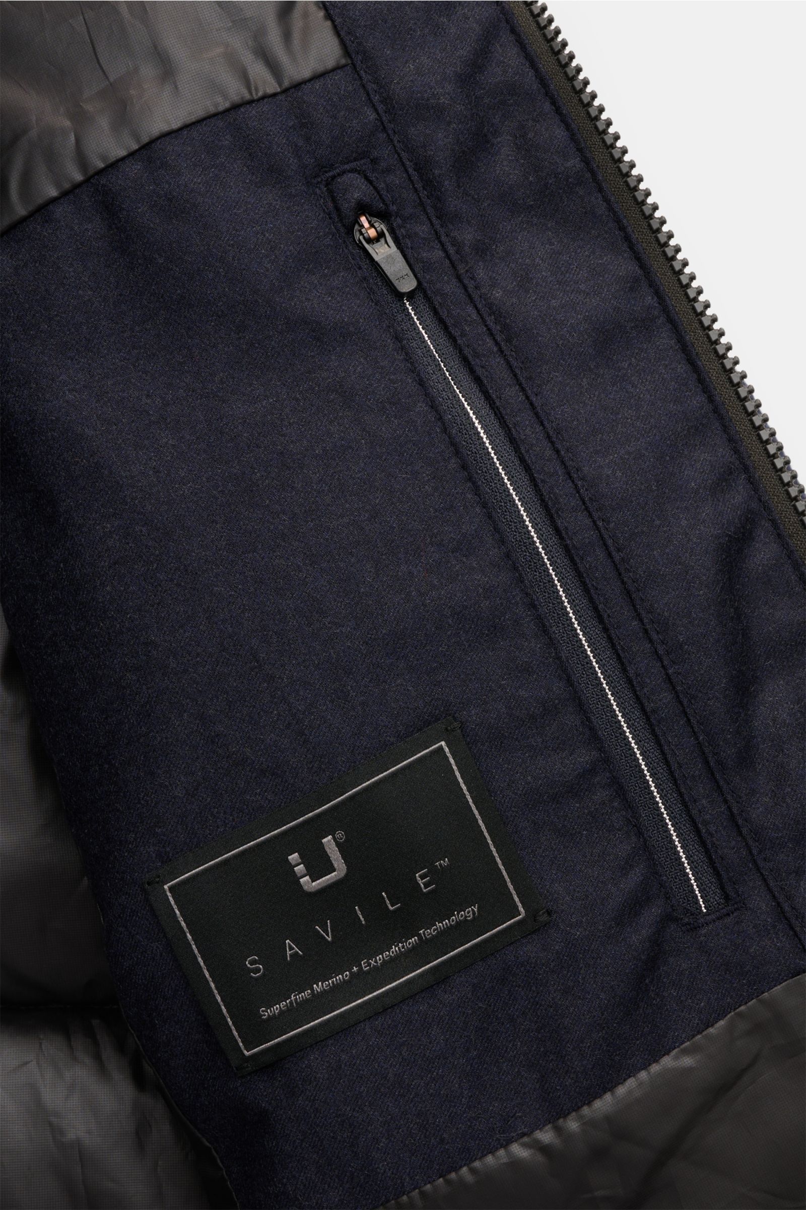 Close-up inside view of the UBR Daunenjacke 'Concord' navy meliert showing soft pure wool fabric, zipper pocket, and Savile label. Urban style meets high-performance with features like soft touch, warm down filling, slim fit, two-way zipper, removable pad