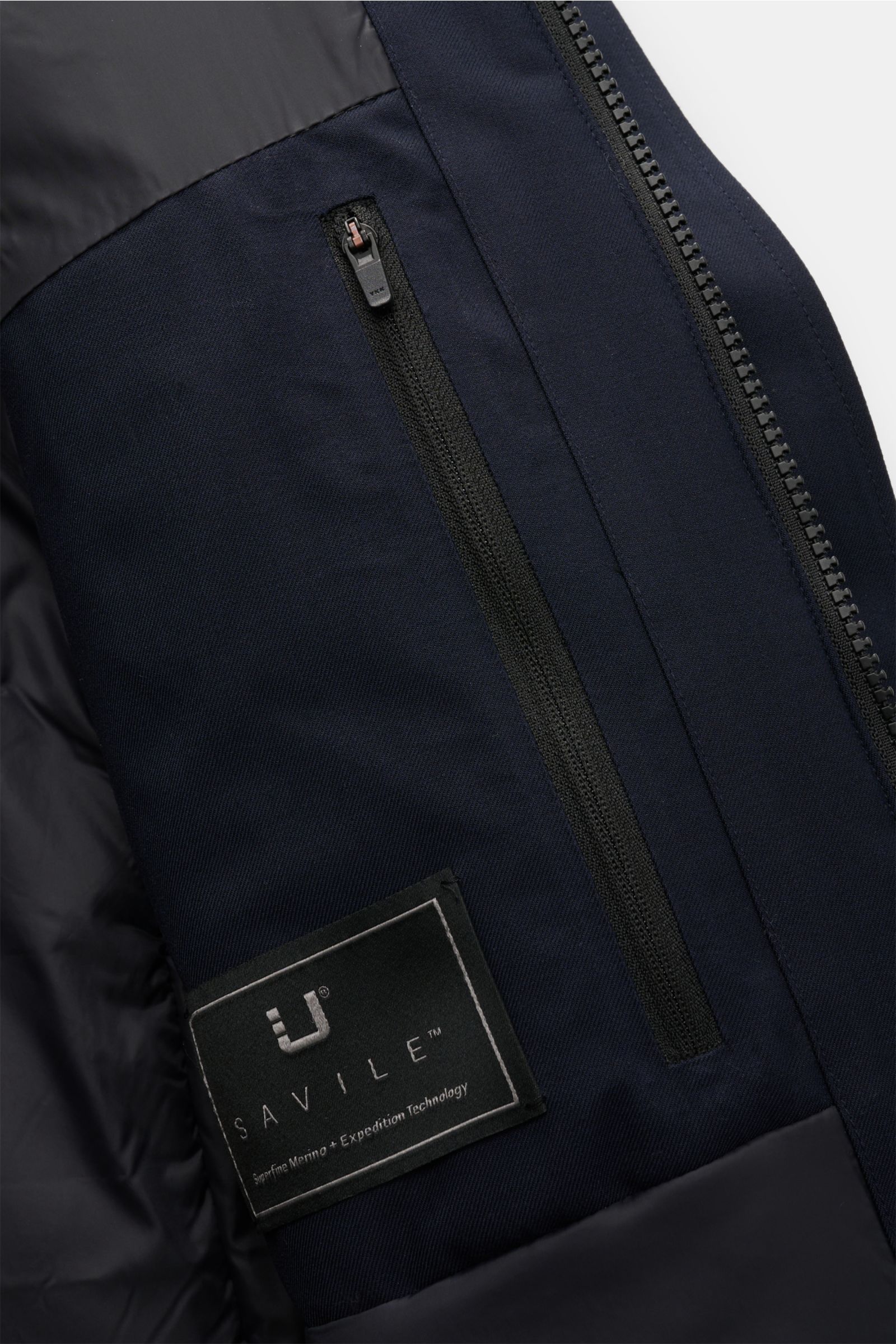 Close-up interior view of the UBR Parka 'Regulator Parka Savile' navy showing a zipped inner pocket and the Savile label, featuring twill Merino wool fabric with Primaloft padding, waterproof membrane, taped seams, and smooth lining, highlighting its func