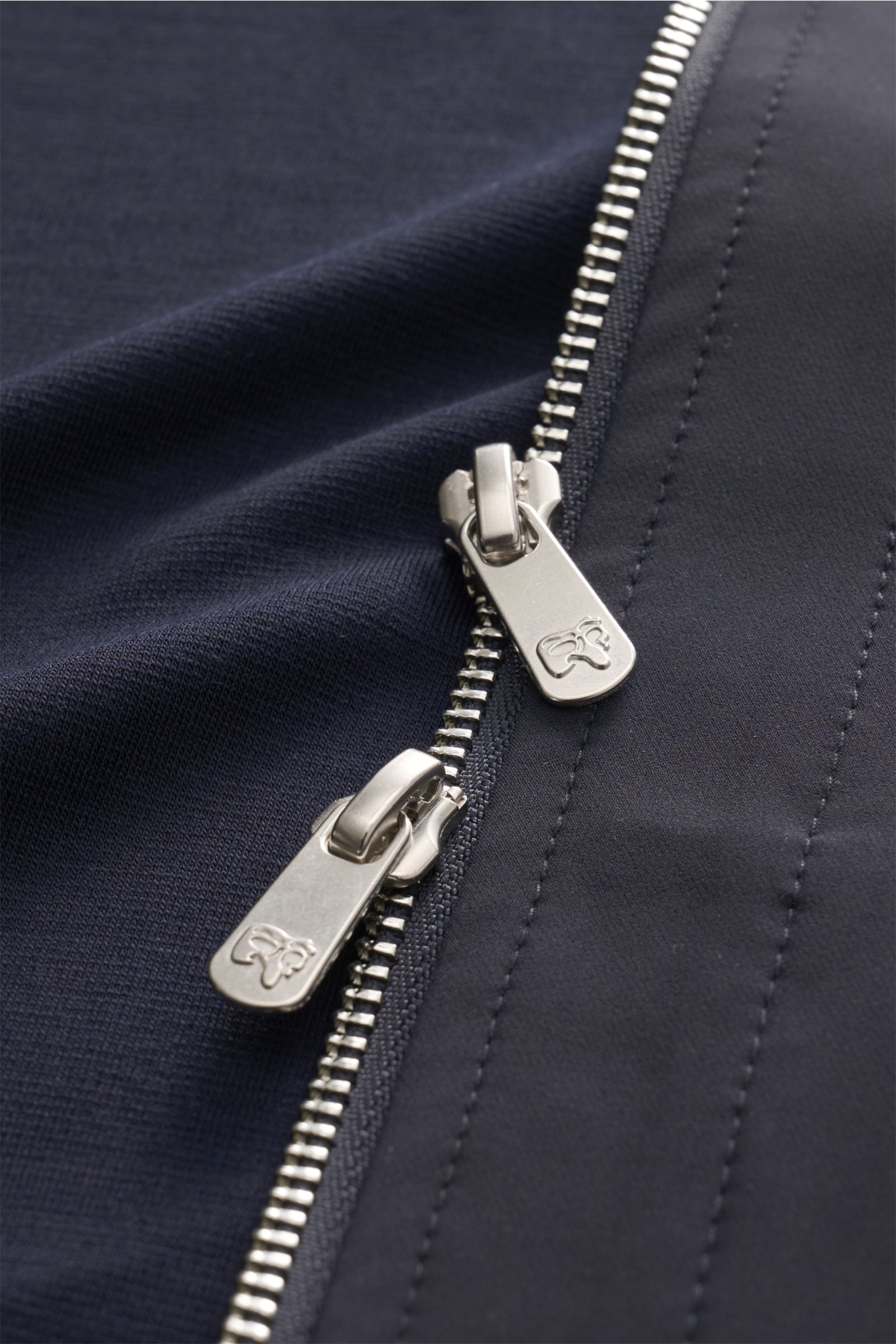Close-up front view of the silver double zipper on the navy Marco Pescarolo Jacke 'Key' navy, showing detailed fabric texture. Ihre sportive Optik verdankt die Jacke 'KEY' von MARCO PESCAROLO den Ärmeln und dem Rückenteil aus Jersey, die der edlen Schu