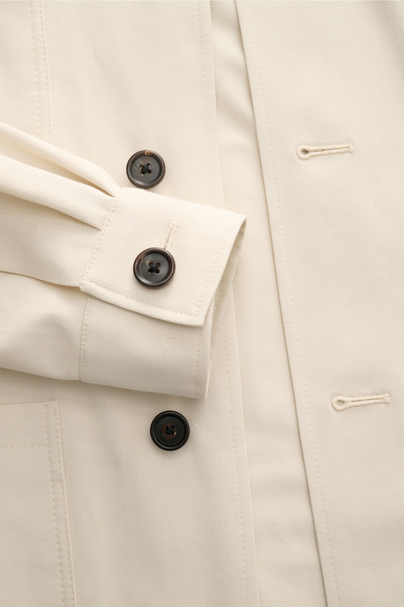 Nahaufnahme der Corneliani Jacke creme aus elastischer Baumwolle mit Slim Fit, Umlegekragen, Manschetten und Knopfleiste, Detail von Ärmeln und Taschen.