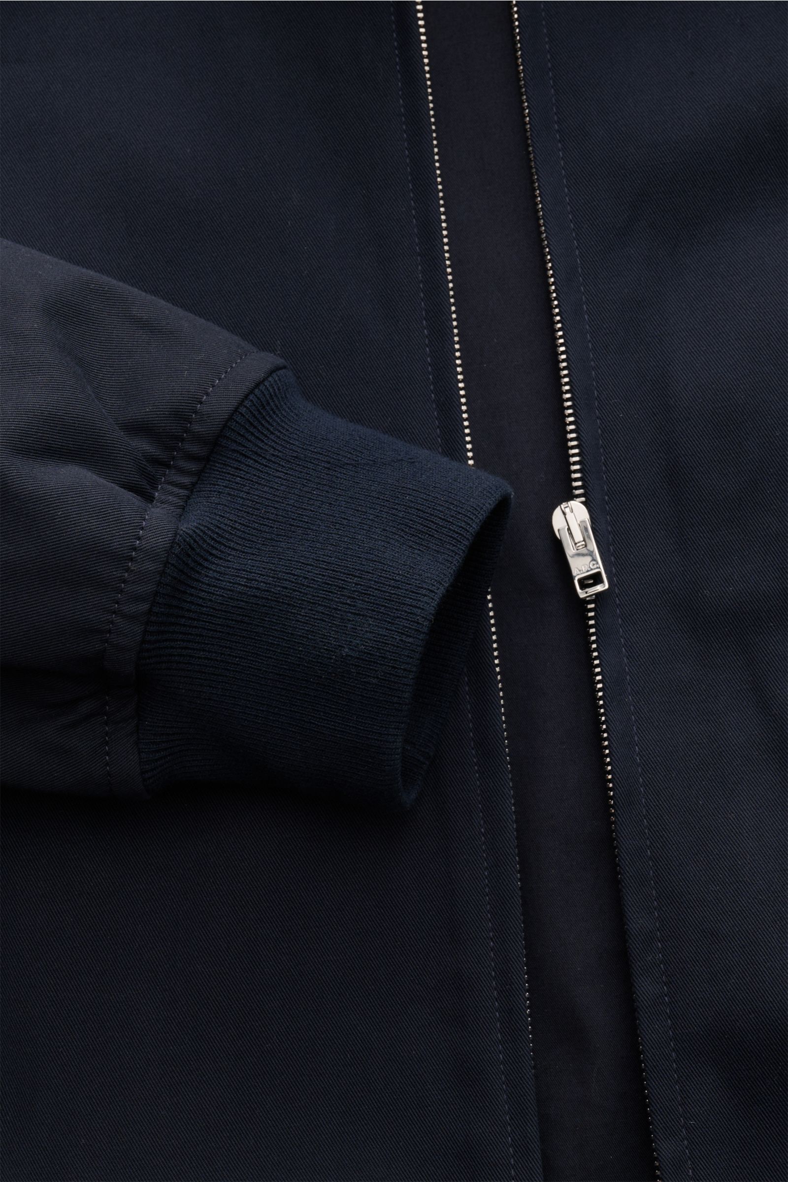 A close-up front view of the A.P.C. Blouson dark navy showing the ribbed sleeve cuff, concealed silver zipper with A.P.C. logo, and dark navy cotton gabardine fabric. Distinctive, urban and clean: This blouson by A.P.C. plays with clear shapes. High-quali