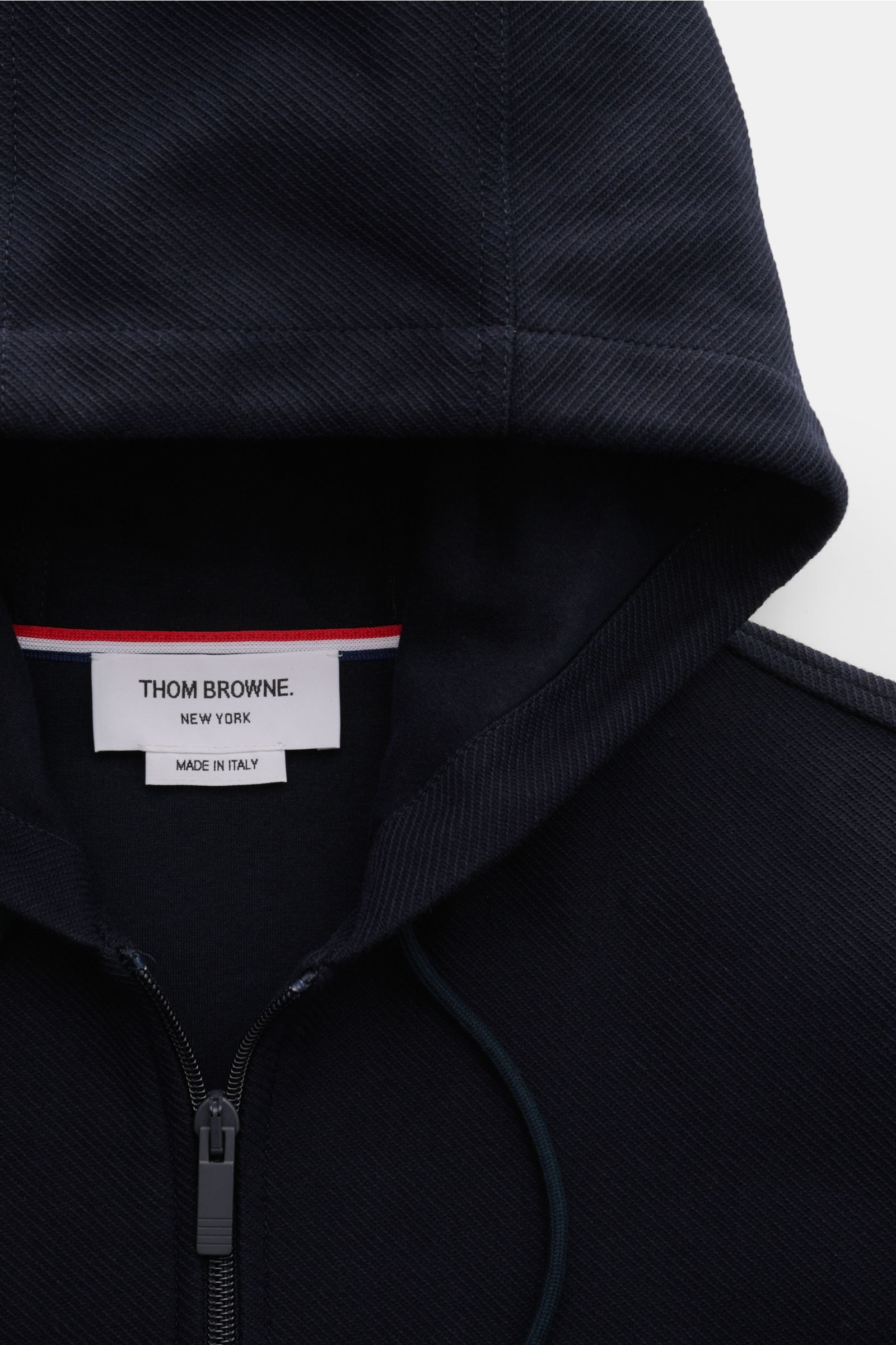 Close-up front view of Thom Browne Jacke navy hoodie in breathable pure cotton with two-way zipper, hood with drawstring, and textured fabric.

Description: Legeres Layering-Piece: Die THOM BROWNE Jacke besticht mit sportiv-zeitlosem Look und wird mit 
