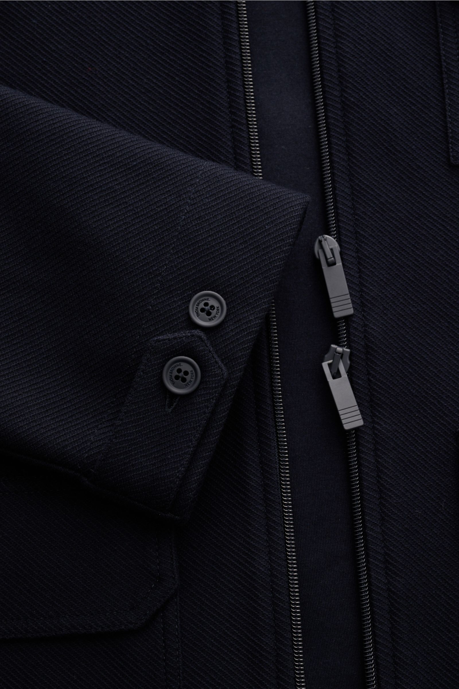 Close-up view of the Thom Browne Jacke navy showing the textured cotton fabric, two-button cuff, and two-way zipper. Legeres Layering-Piece: Die THOM BROWNE Jacke besticht mit sportiv-zeitlosem Look und wird mit ihrem atmungsaktiven Baumwollmaterial zu