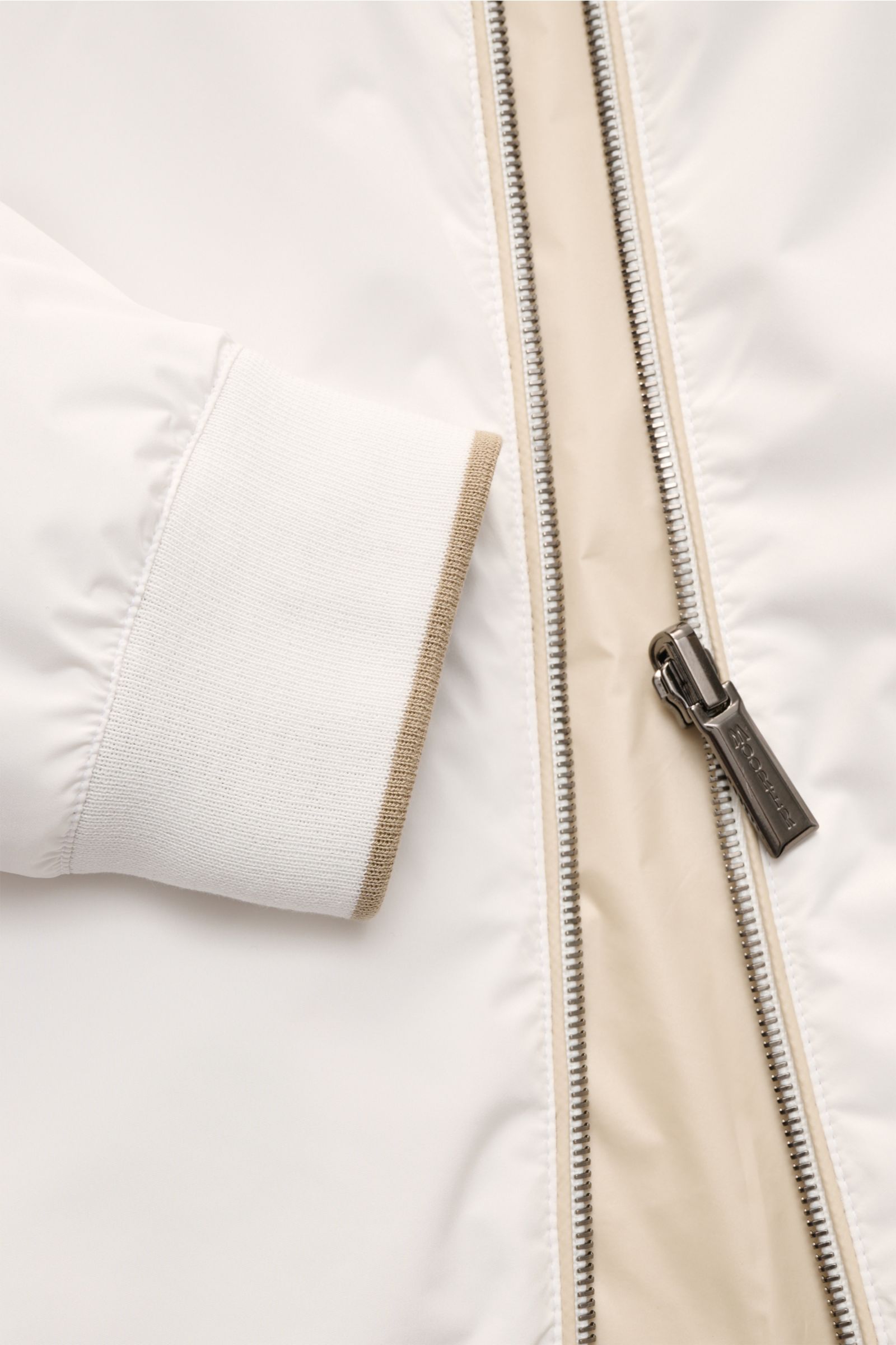 Close-up front view of the Moorer Wende-Blouson 'Dennys' offwhite/beige, showing smooth microfiber fabric, ribbed elastic cuff with beige trim, and water-repellent zipper with branded pull. Funktionaler Outdoor-Luxus: Mit seinem wendbaren Design vereint d